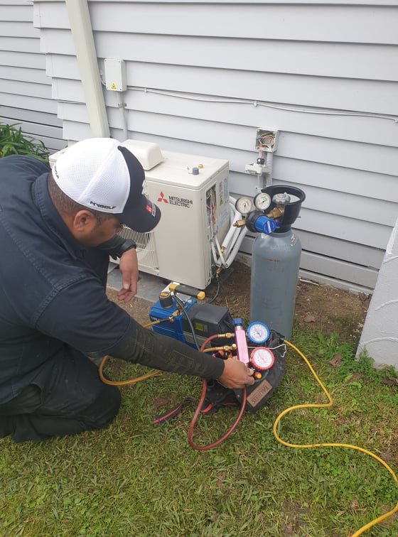Technician using manifold gauges on an air conditioning unit outside house.