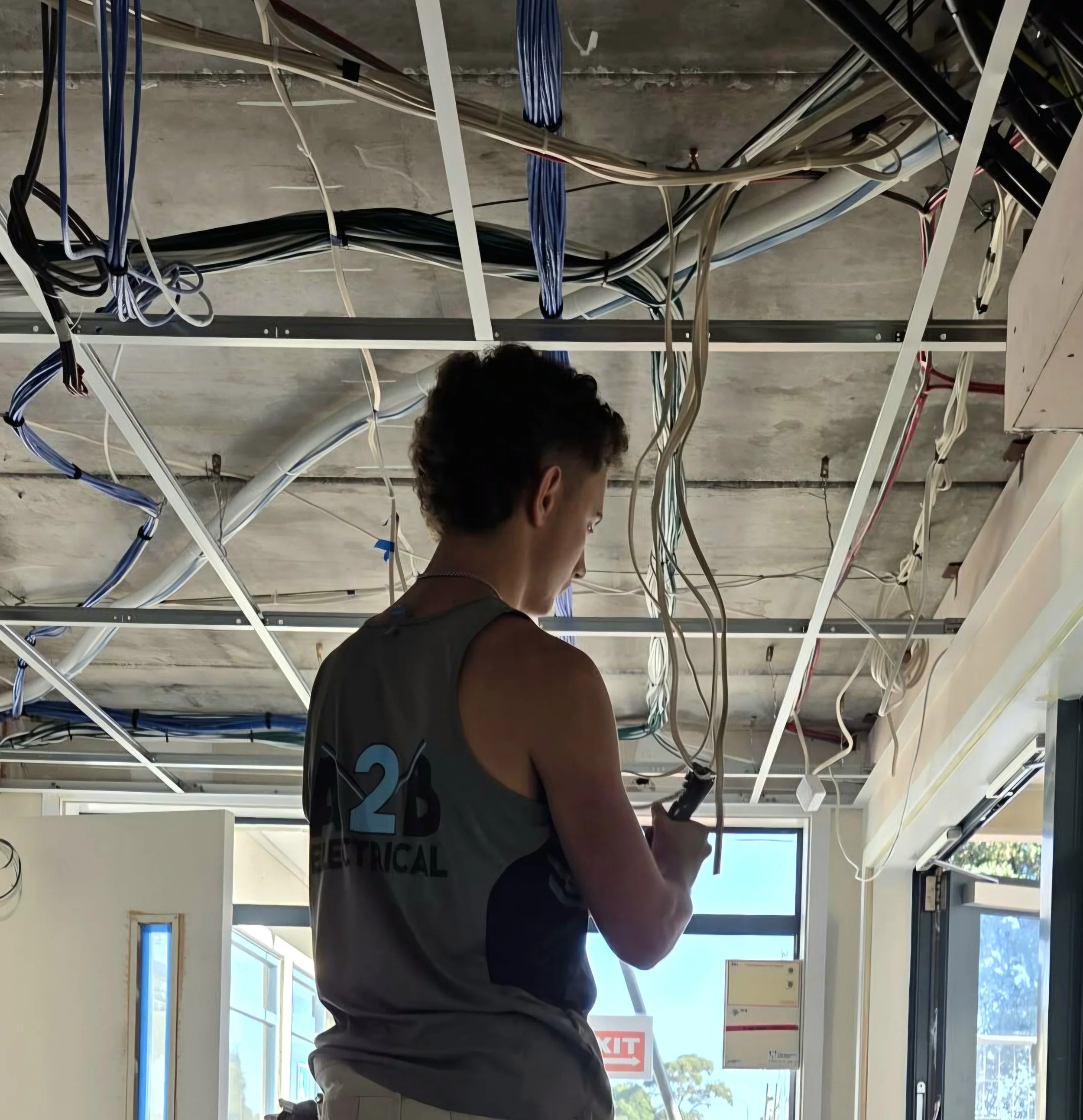 Person installing or inspecting electrical wiring in a commercial or industrial building with a focus on cables and electrical infrastructure.