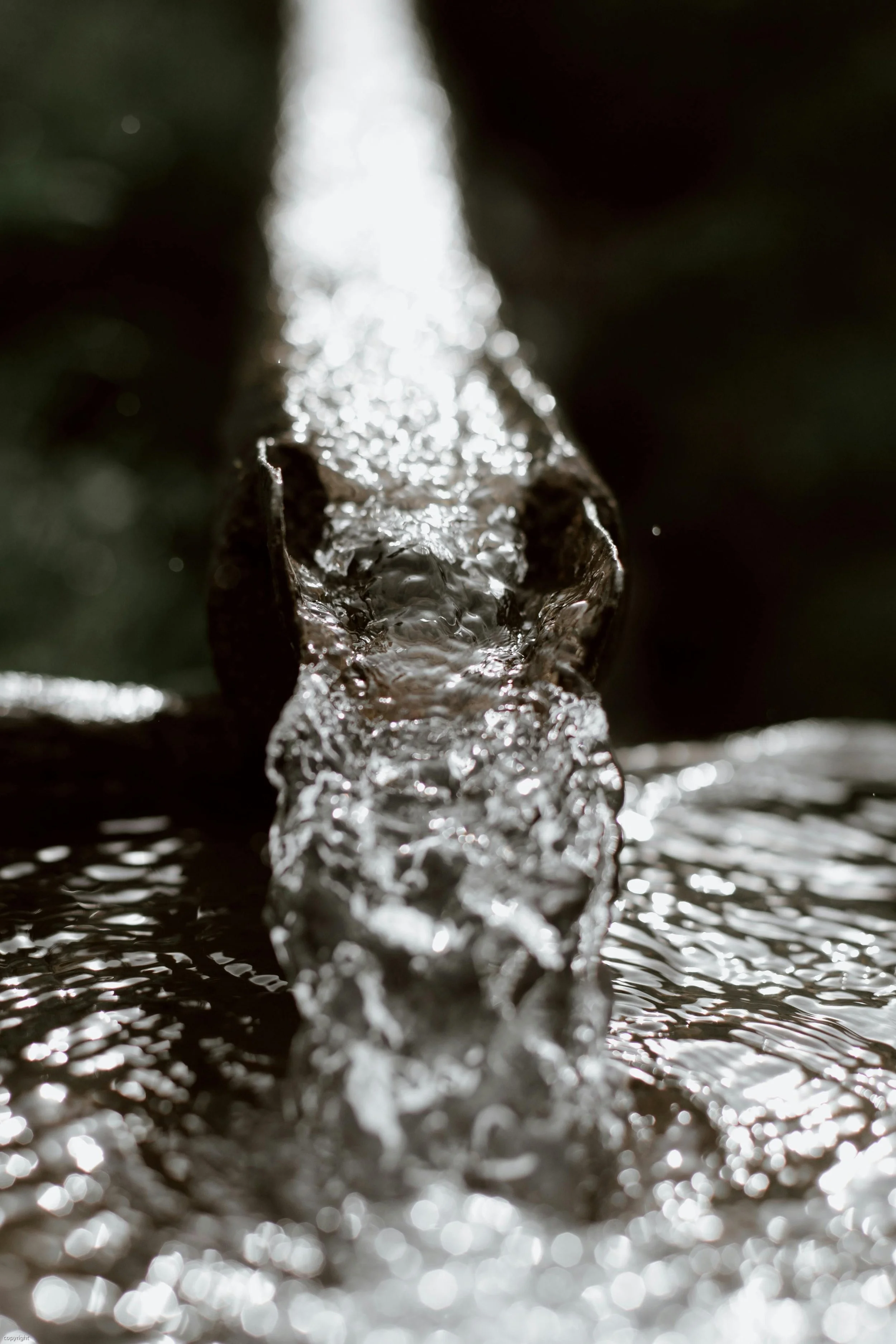 Close-up of flowing water in a narrow stream or crevice, with sunlight reflecting off the water's surface.