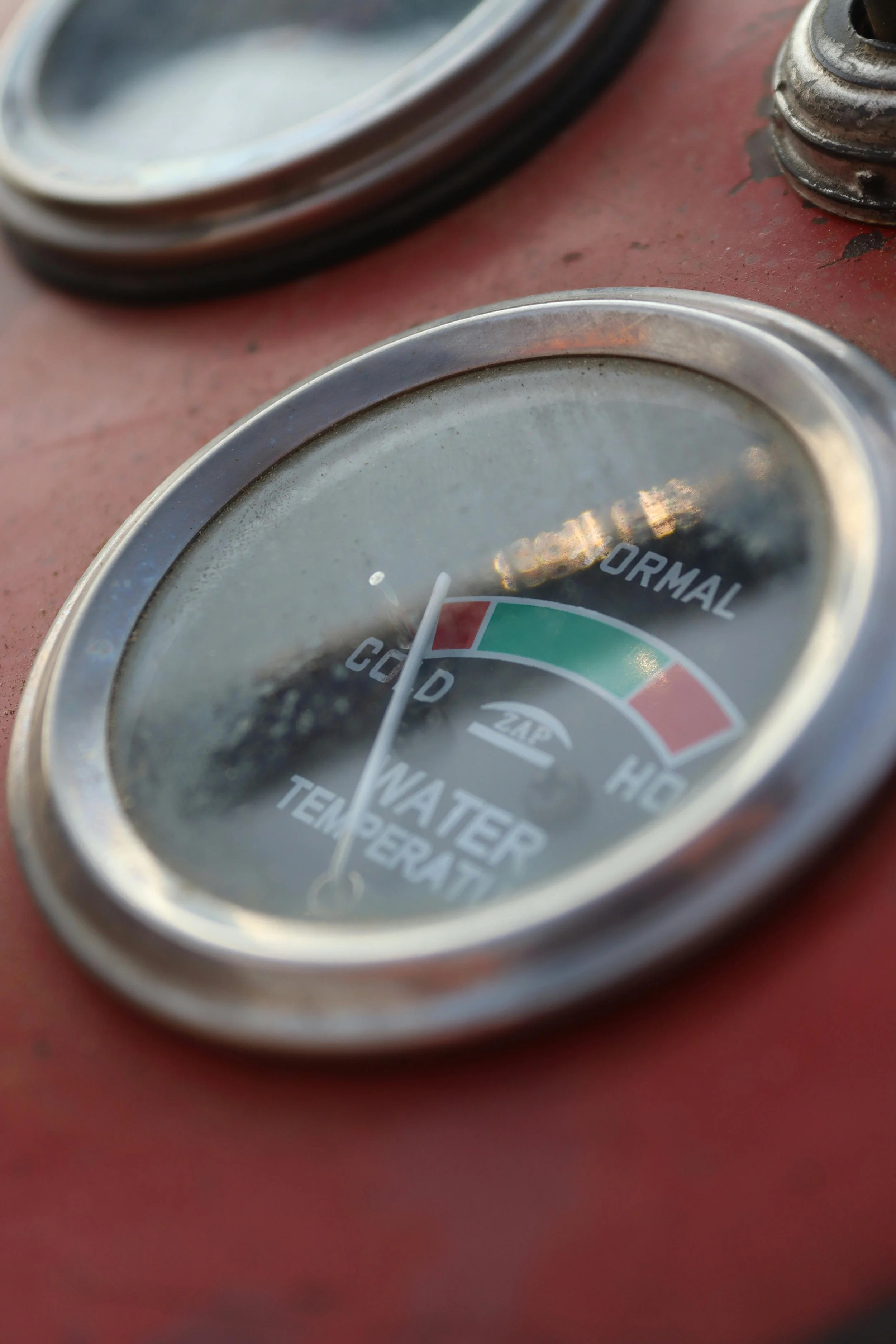 Close-up of a gauge indicating temperature or pressure, with a red surface and a partially visible glass cover.