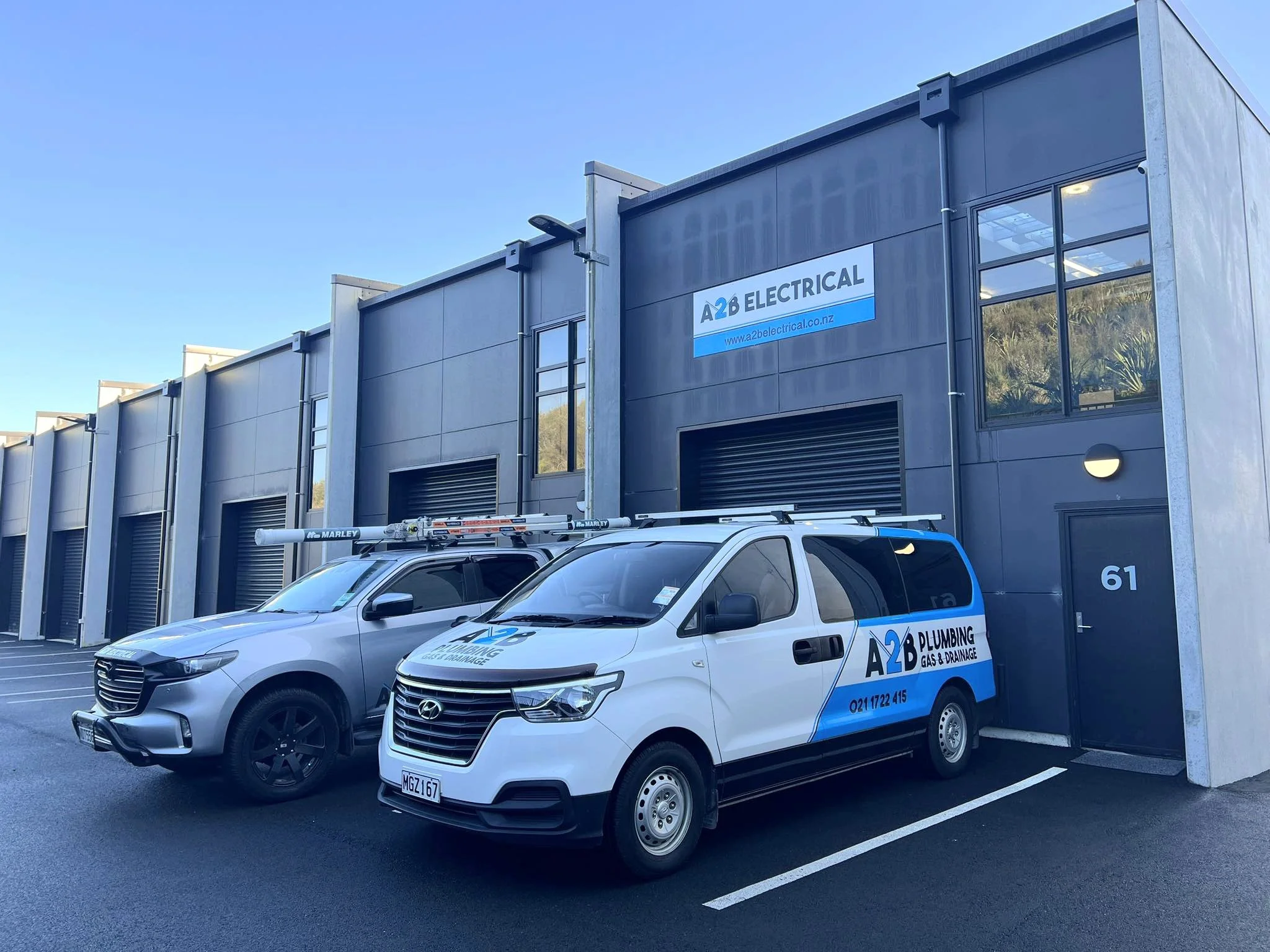 Commercial building with a sign for A2B Electrical, and a parked white Hyundai vehicle with company branding in a parking lot under a clear blue sky.