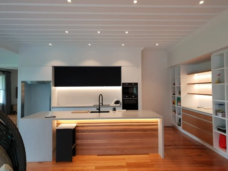Modern kitchen with white island, wooden accents, built-in oven, and open shelving.