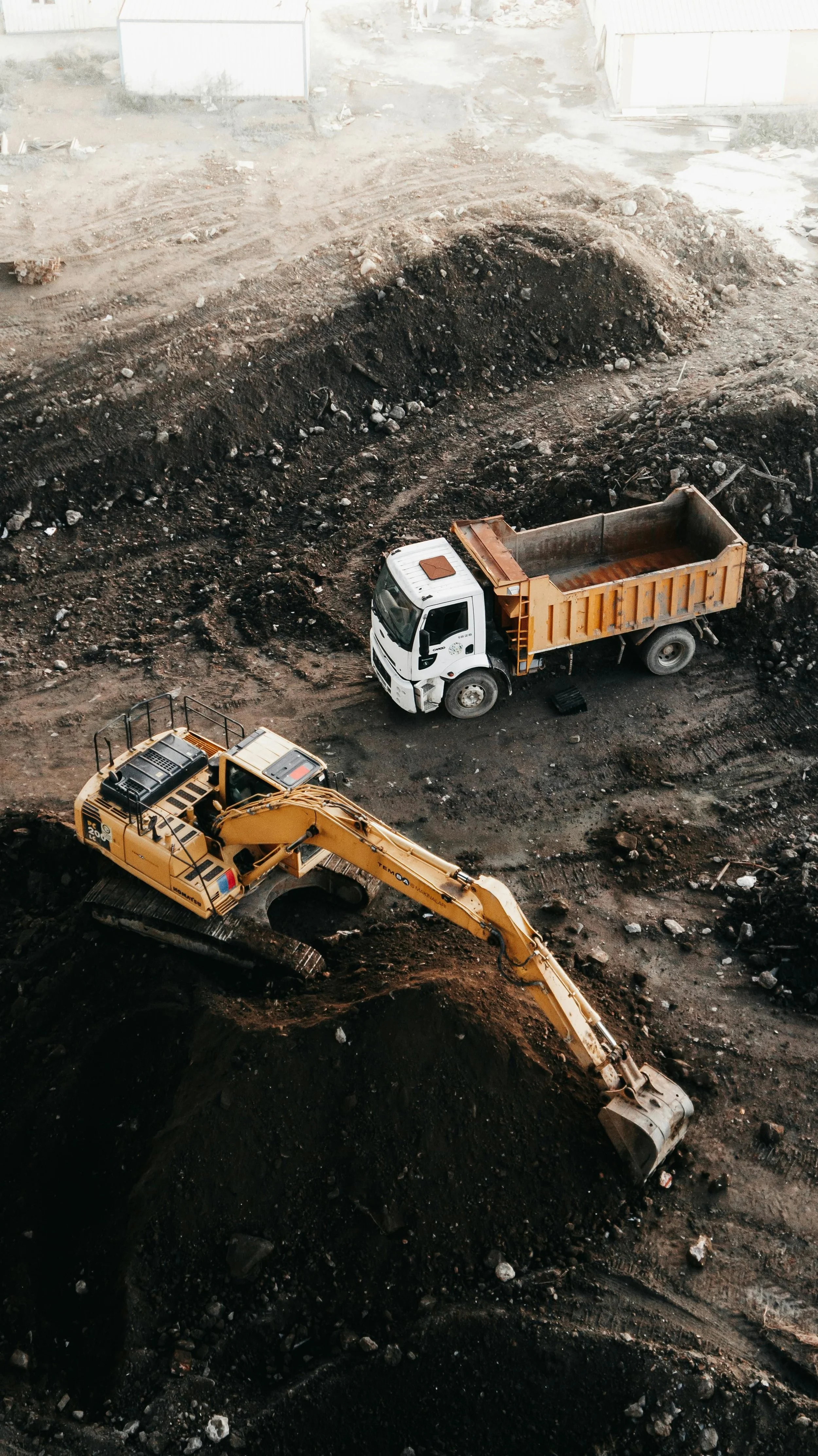 Construction site with excavator and dump trucks working on earth and rock excavation.