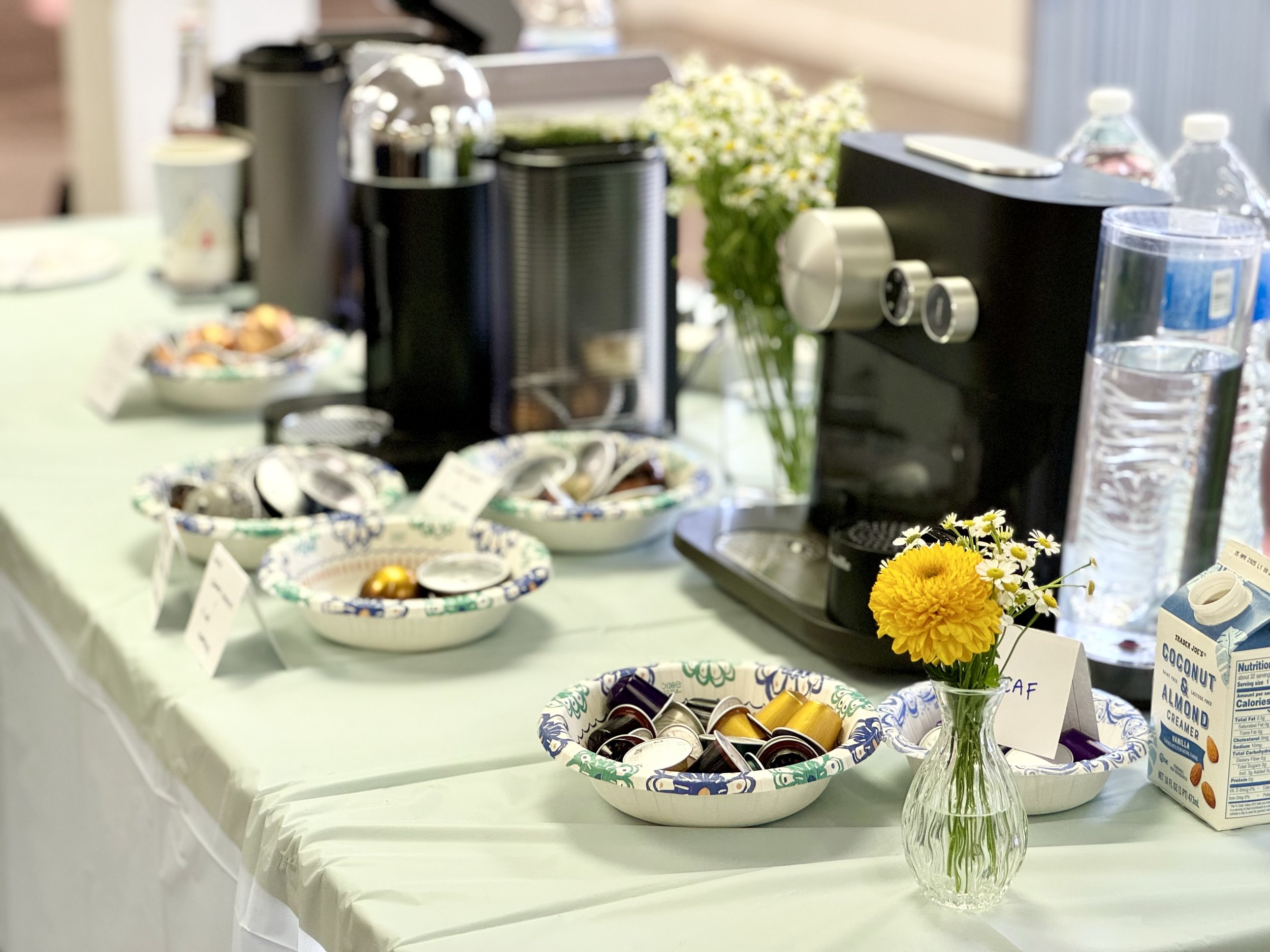 Display of snack containers on a table with a floral arrangement featuring yellow and white flowers in a glass vase.