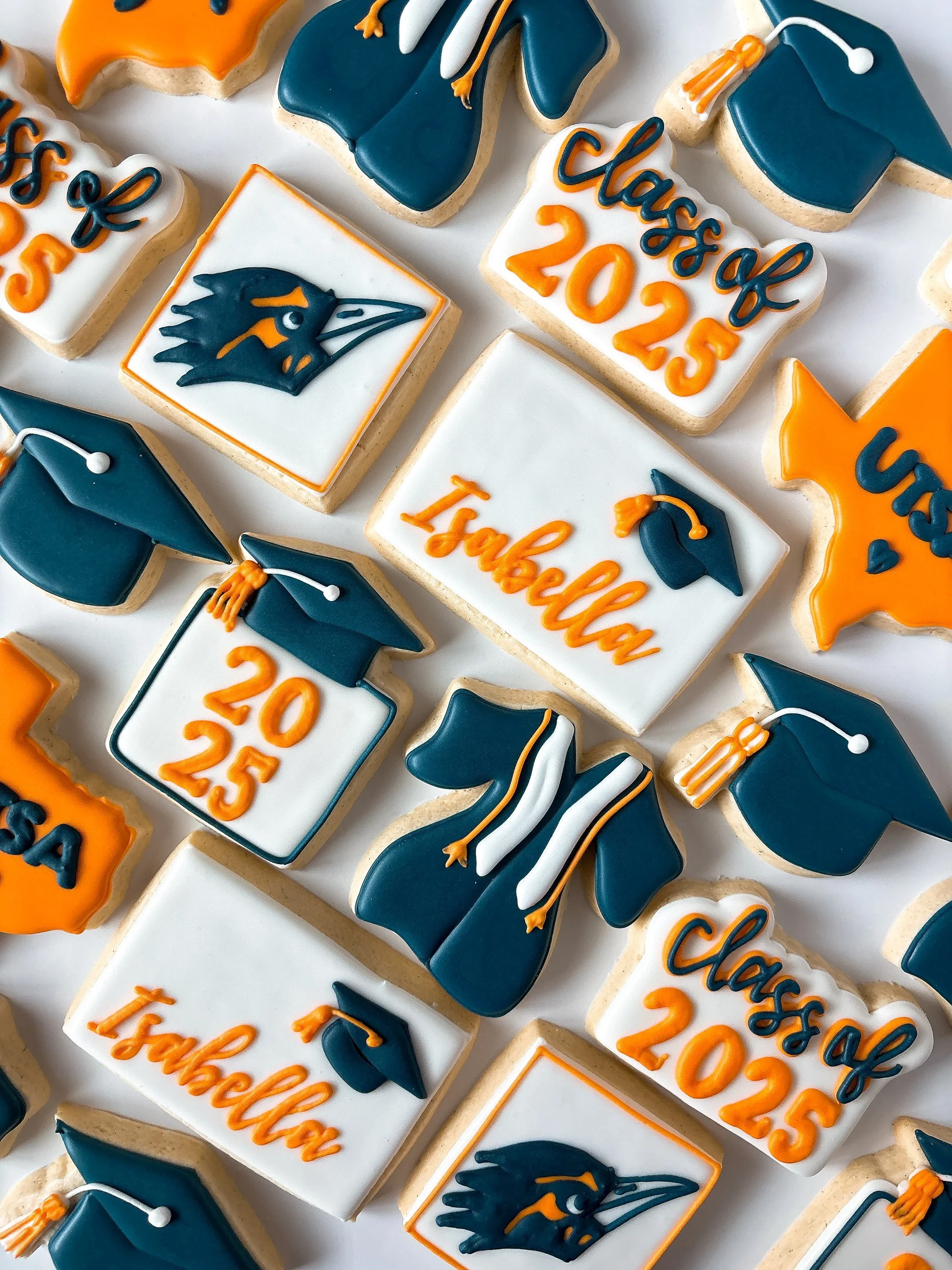 Decorated cookies for a graduation celebration with blue, orange, and white icing, featuring graduation caps, the university's mascot, and text reading 'Class of 2023' and '1st Grad'.