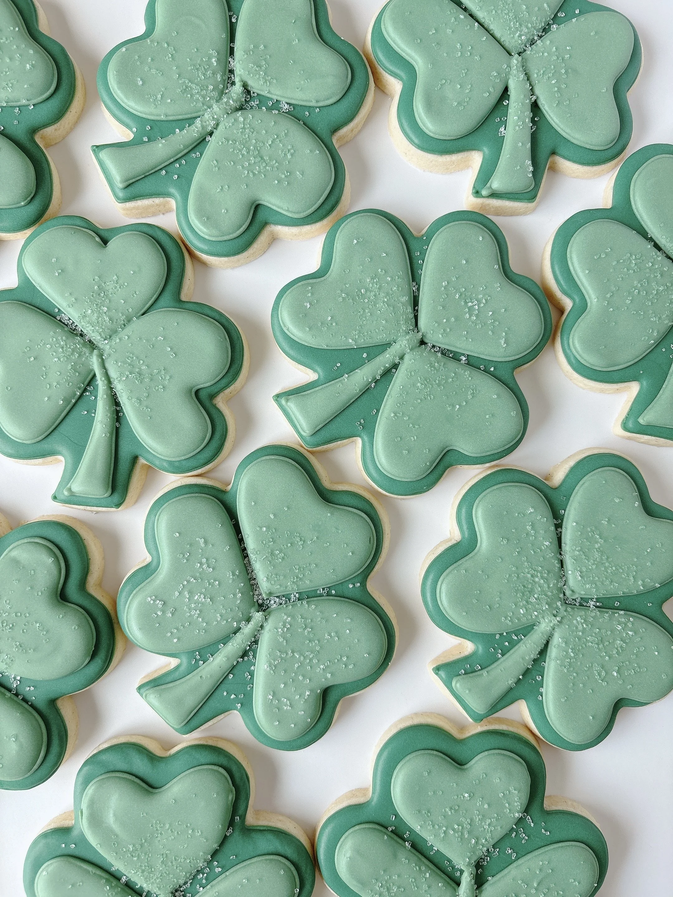 Cookies decorated with green icing shaped like shamrocks and four-leaf clovers, sprinkled with sugar crystals.