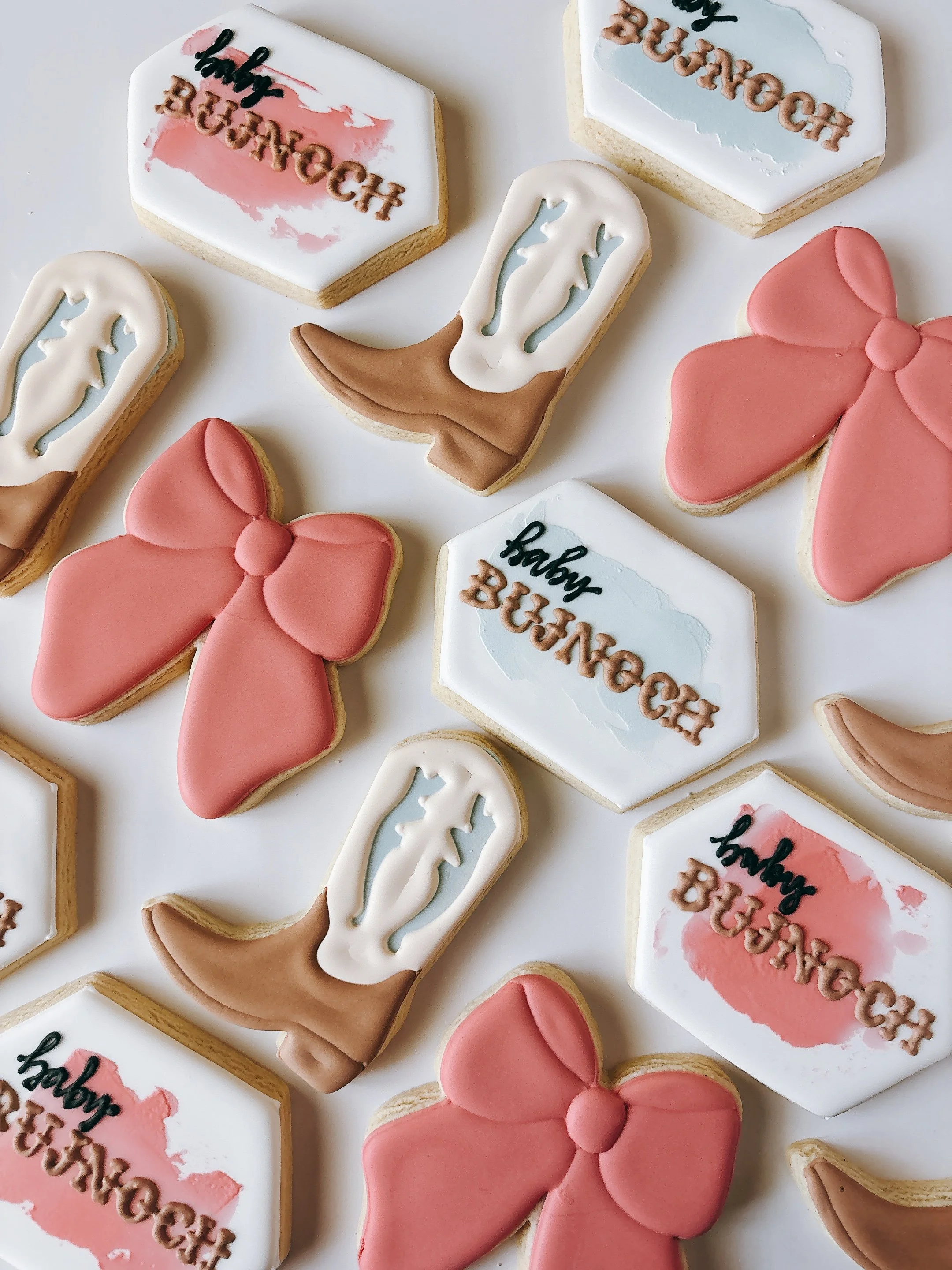 Decorated cookies for a birthday celebration, featuring bows, the phrase 'happy birthday' in icing, and pastel pink, white, and blue colors.