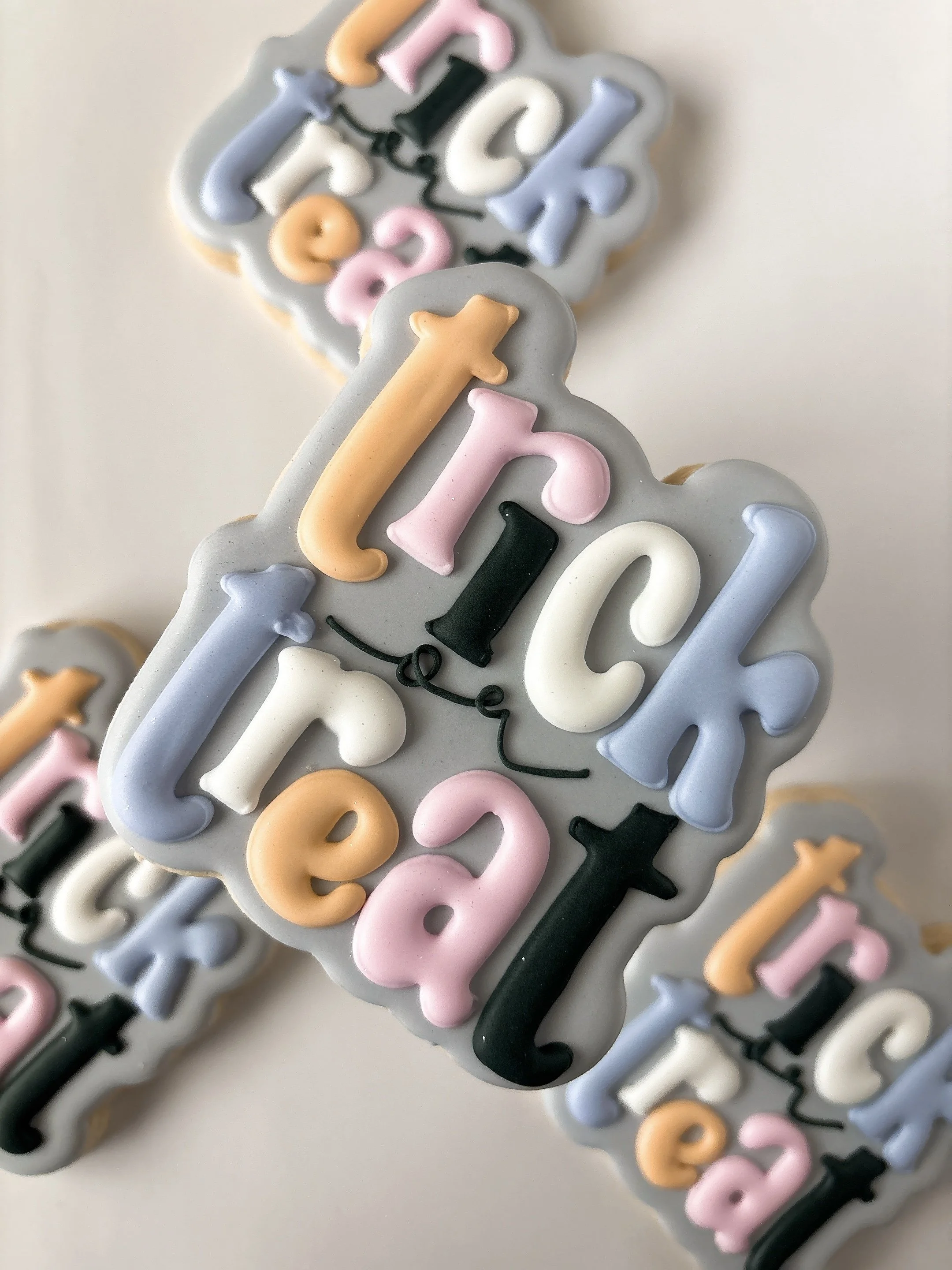 Colorful number-shaped cookies with pastel colors including pink, white, blue, peach, and black, arranged on a lightly frosted surface for a birthday celebration.