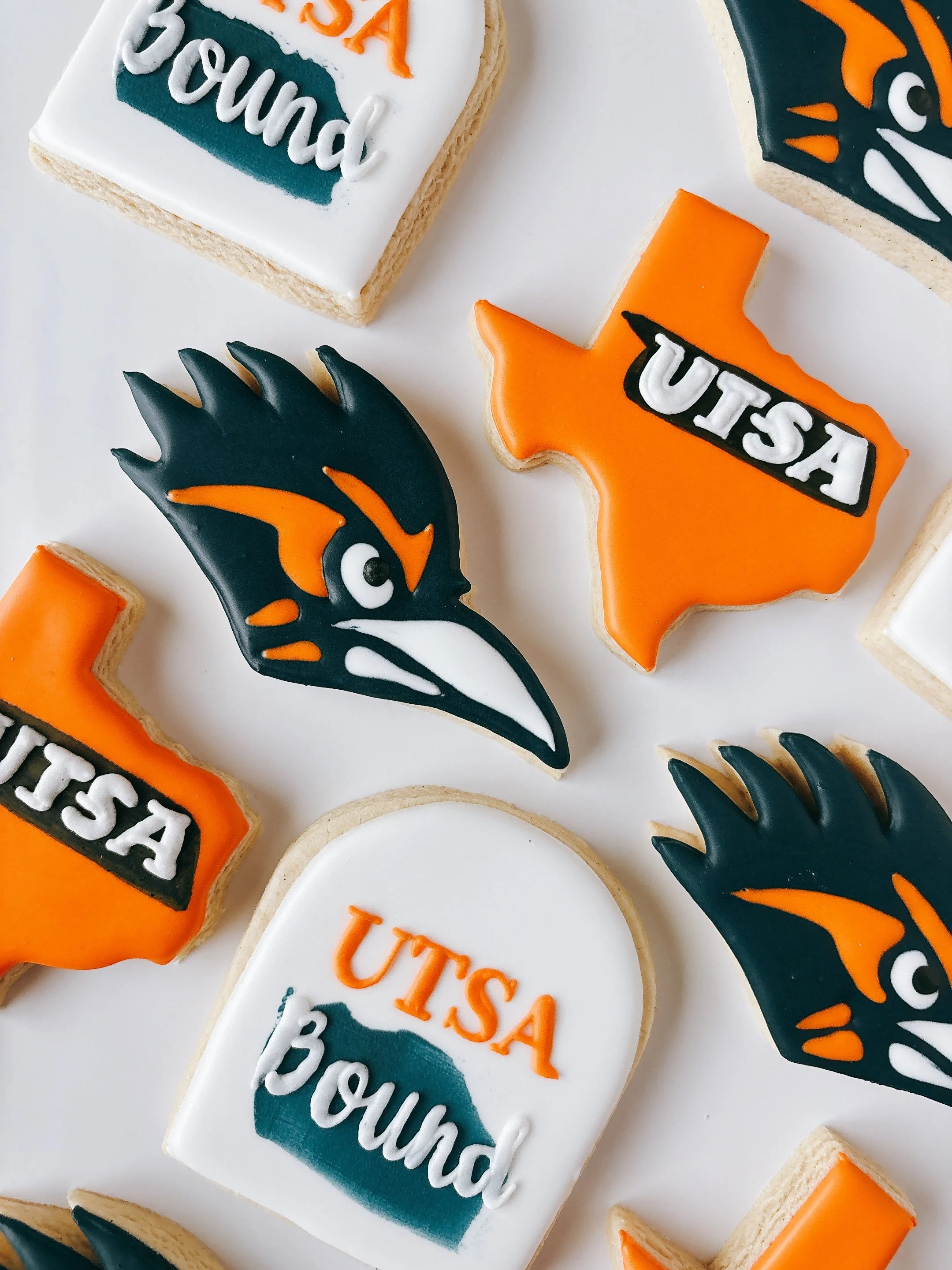 Cookies decorated with slogans and logos, including a black chicken head with orange and white accents, and cookies with the words ''UTA'' and ''BOUNC'' for Texas.