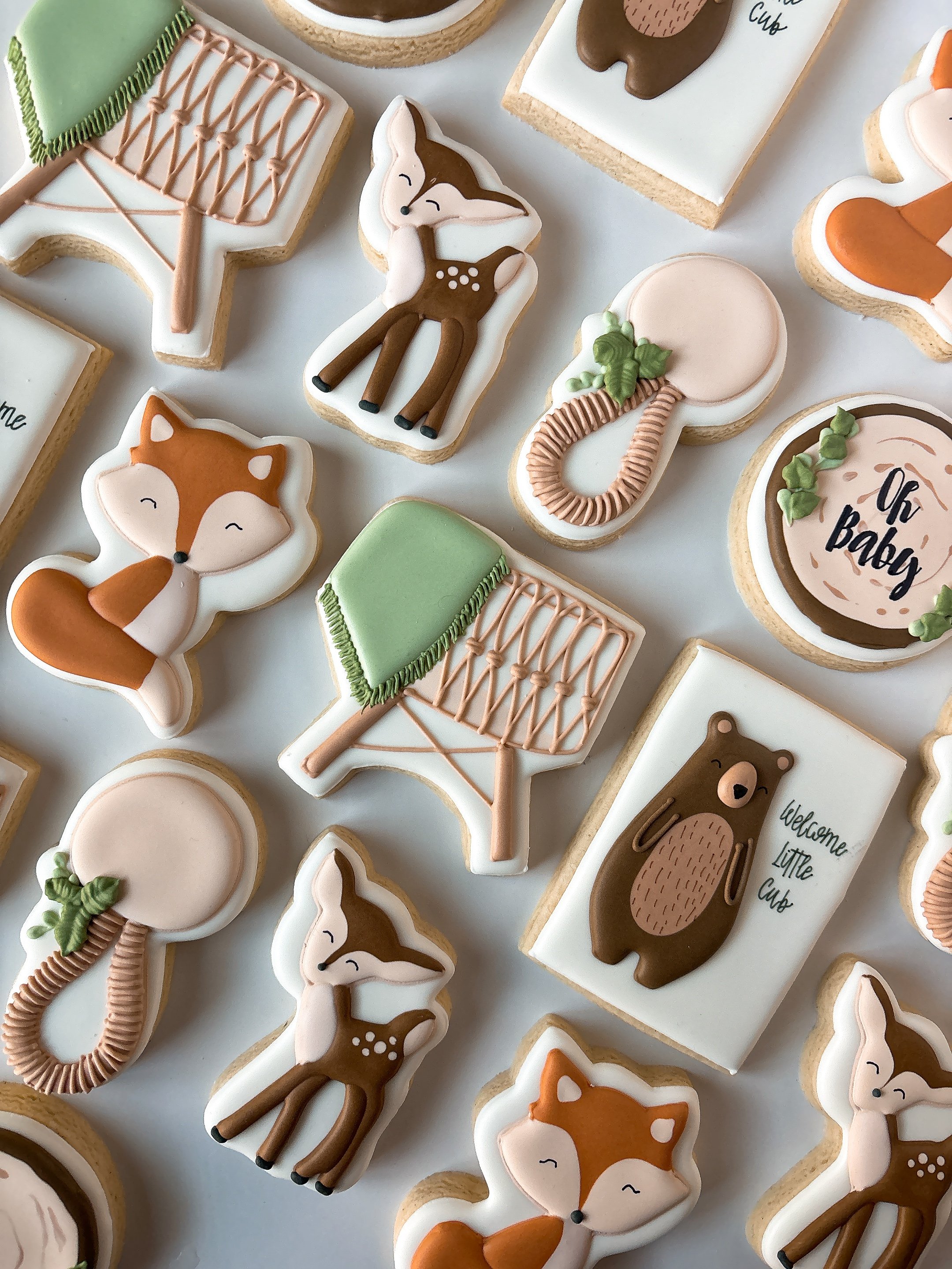 Decorative cookies shaped like foxes, bears, leaves, and speech bubbles, decorated with pastel-colored icing with woodland theme details.