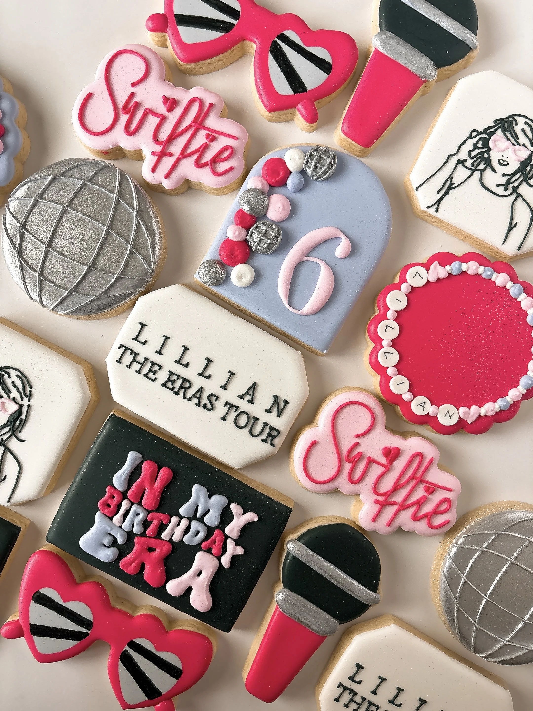Decorative cookies themed around a makeup artist's tour, with designs including a makeup brush, lipstick, sunglasses, and the phrase 'Surprise' in pink icing, along with numbered countdown cookies and a geometric-patterned sphere