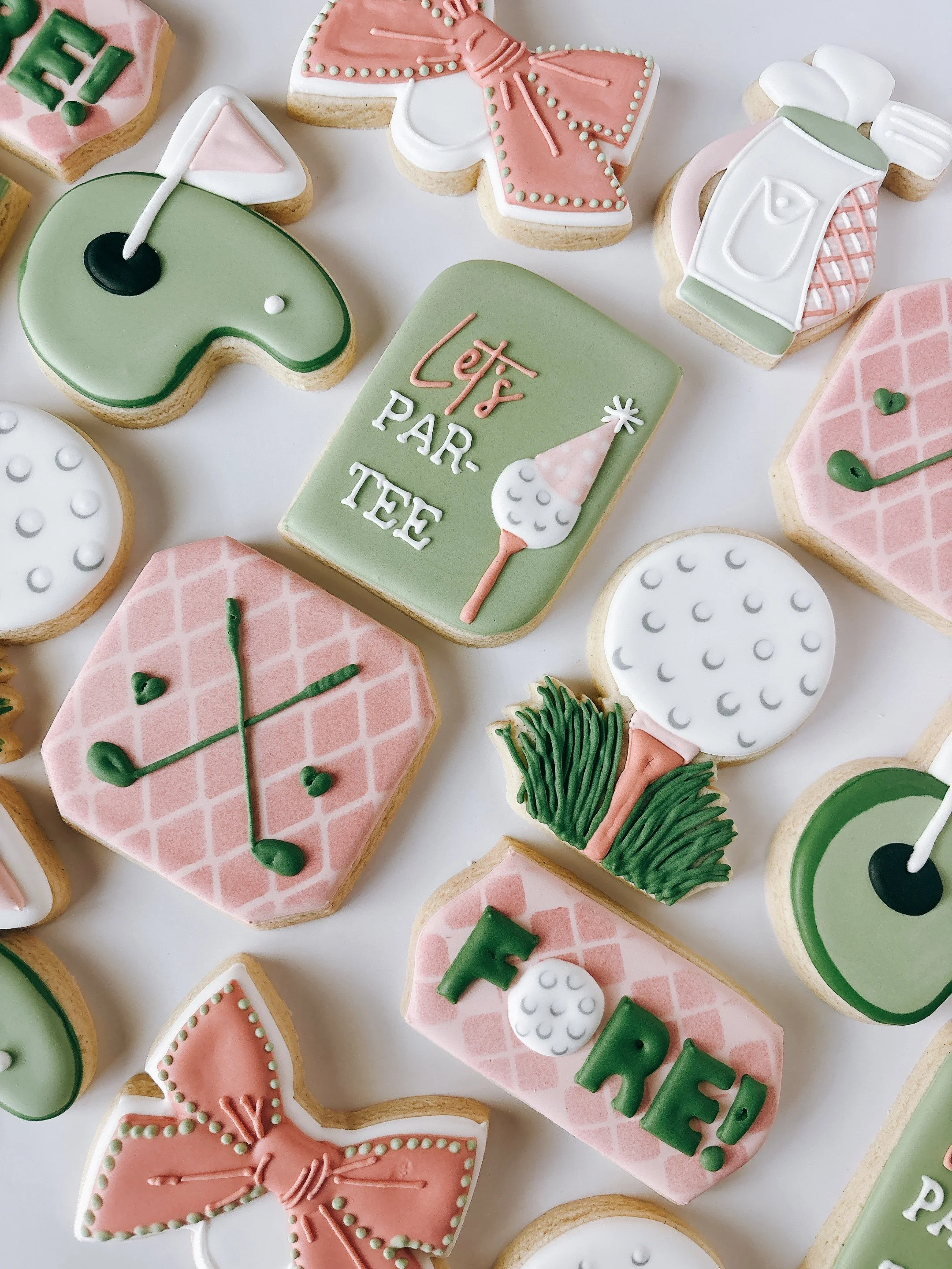 Festive cookies decorated with pastel green, pink, and white icing. Designs include a golf club, a golf ball, a golf tee, a gift box with the word "Let's" and "Par Tee," and a pink bow.