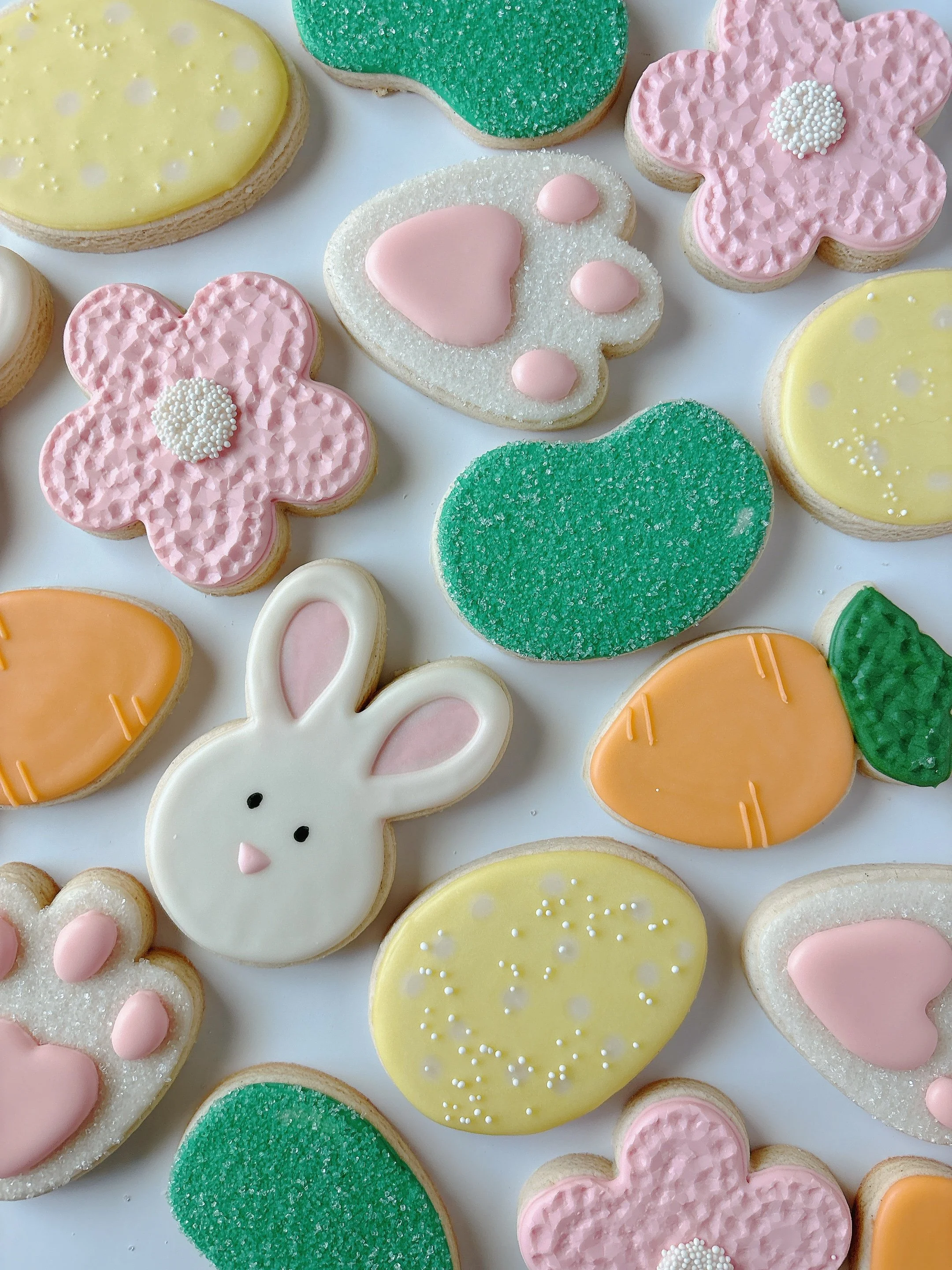 Assorted decorated cookies in Easter-themed shapes including bunny, flowers, eggs, and hearts with pastel icing and sprinkles.