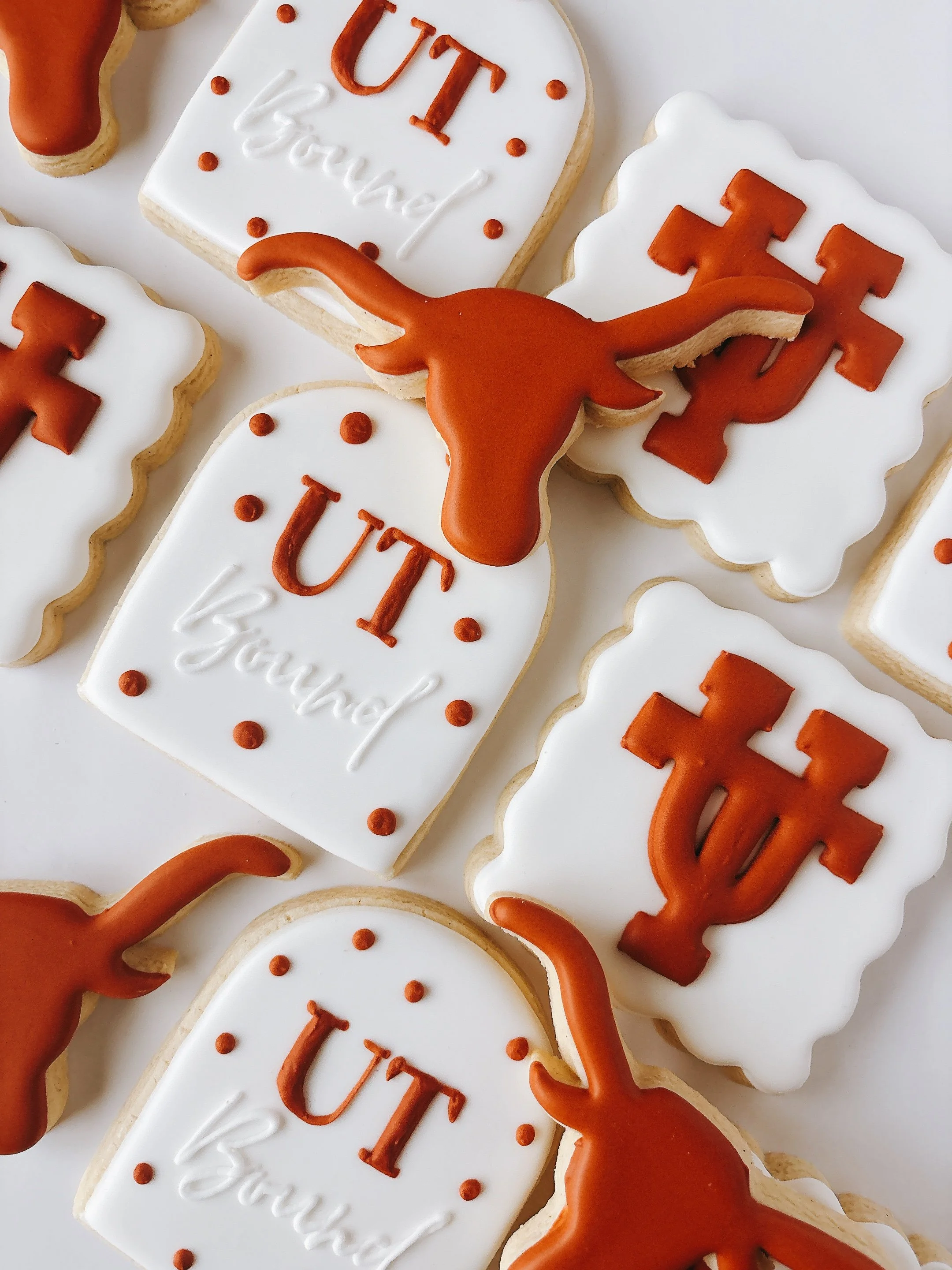 Decorated cookies with white icing, orange melted icing along the borders, and orange lettering spelling 'UT' and 'Love' with small orange dots and a long orange icing shape.