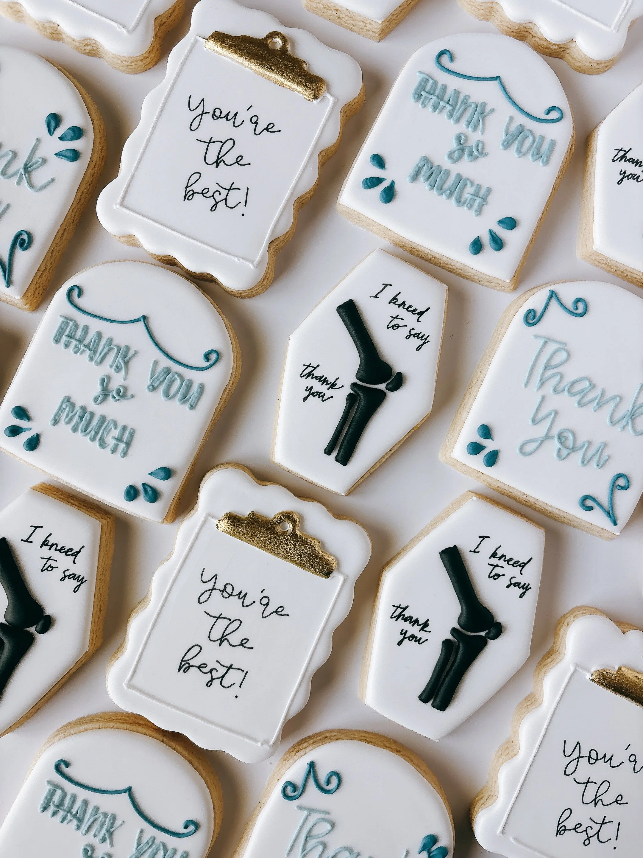 Collection of decorated cookies with messages of gratitude and thanks for mothers. The cookies are rectangular, oval, and sheep-shaped, decorated with white icing and blue or black writing. Some cookies have messages like "You're the best!" and "Than