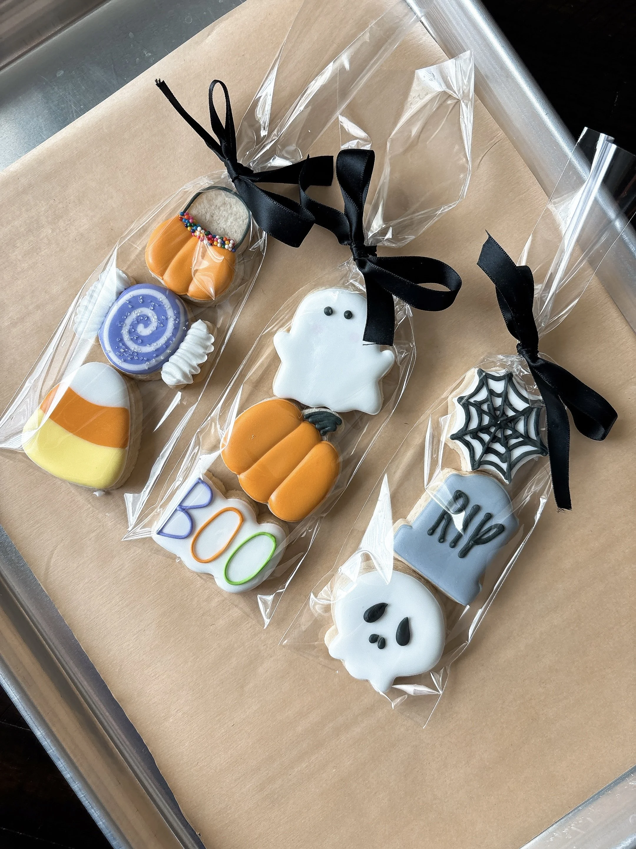 Halloween-themed decorated cookies in clear packaging with black ribbons on a table.