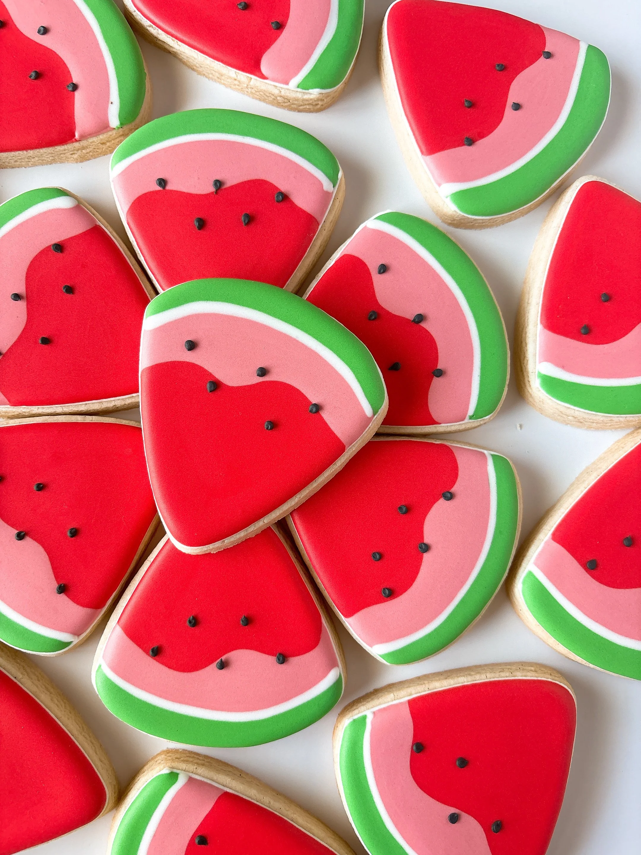 Decorative watermelon-shaped cookies with red, pink, green, and white icing and small black icing seeds.