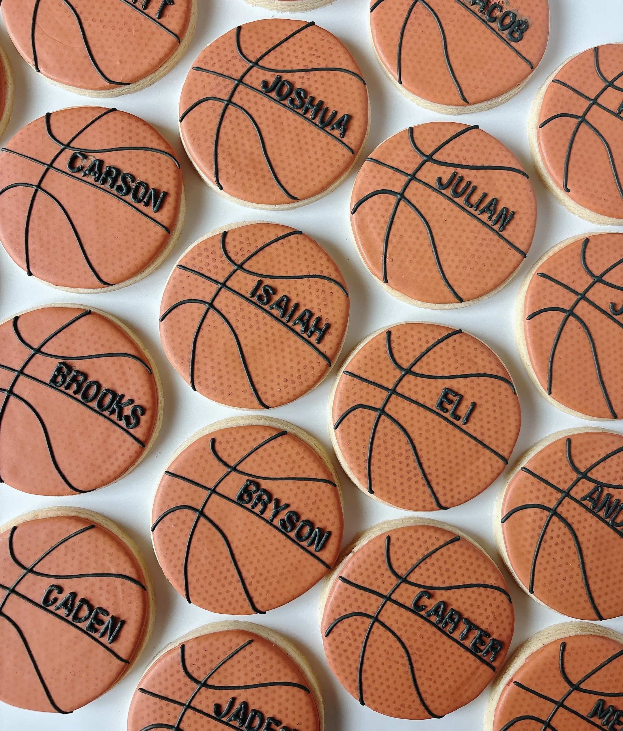 Cookies decorated as basketballs with orange icing, black icing lines, and the names of basketball players in black icing.