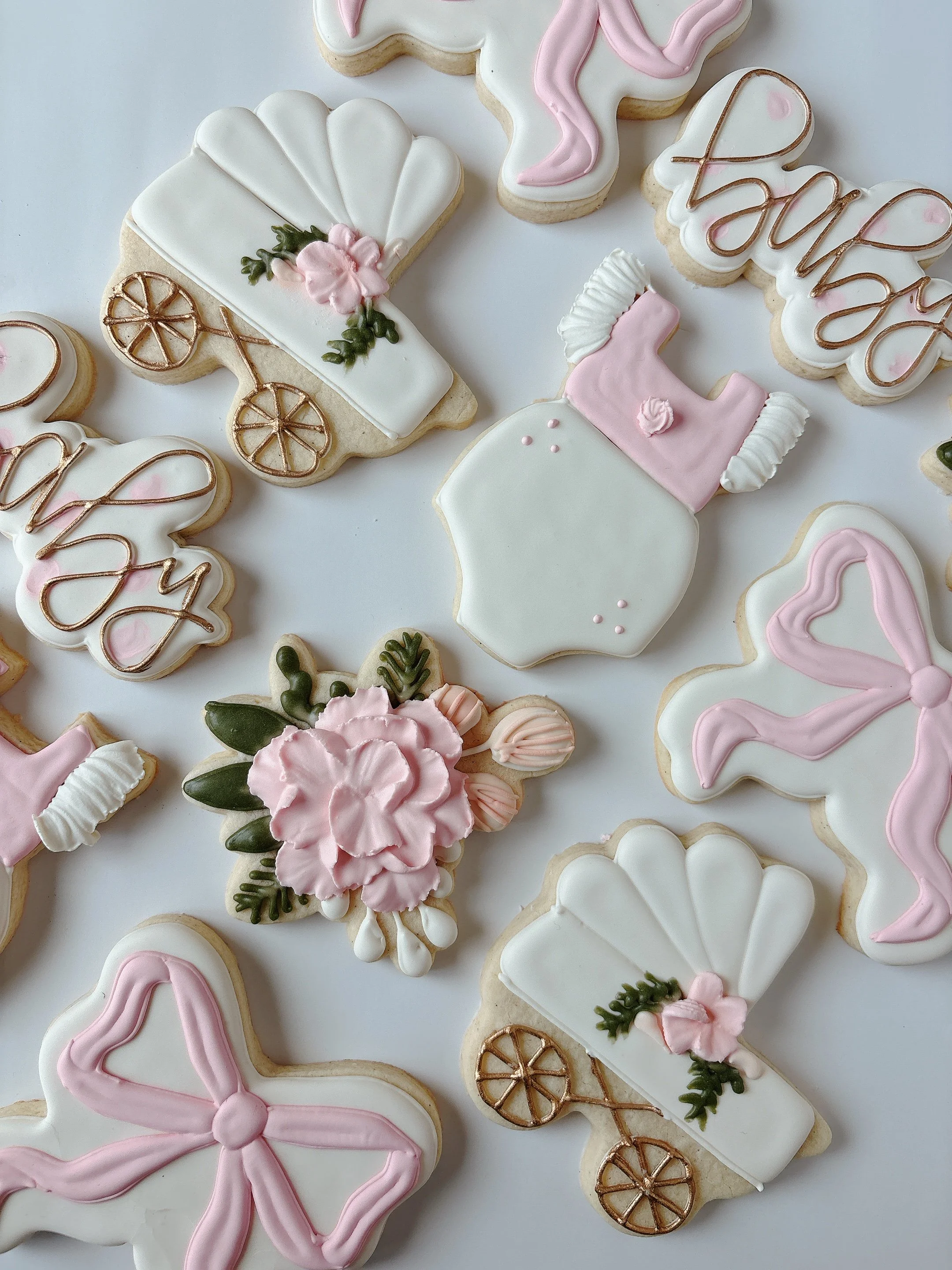 Decorated cookies in pastel pink and white colors, with designs including a baby carriage, a bow, a letter B, and a word 'love' with intricate icing and piping.