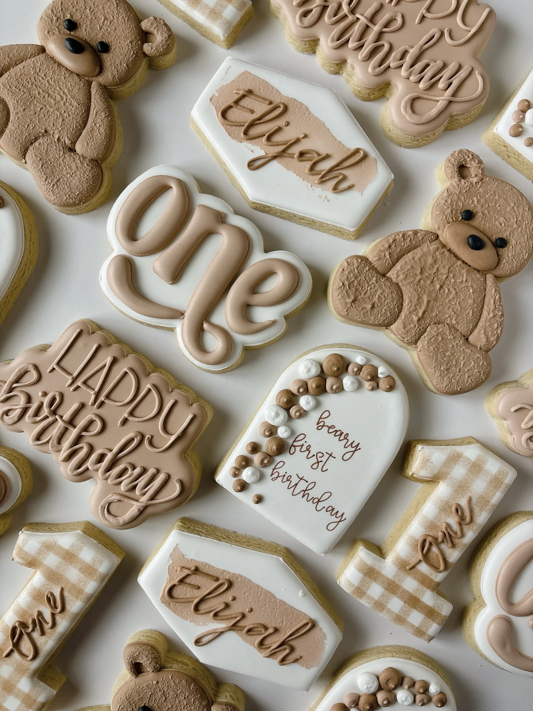 Assorted decorated cookies with birthday messages, teddy bear shapes, and various embellishments arranged on a white surface.