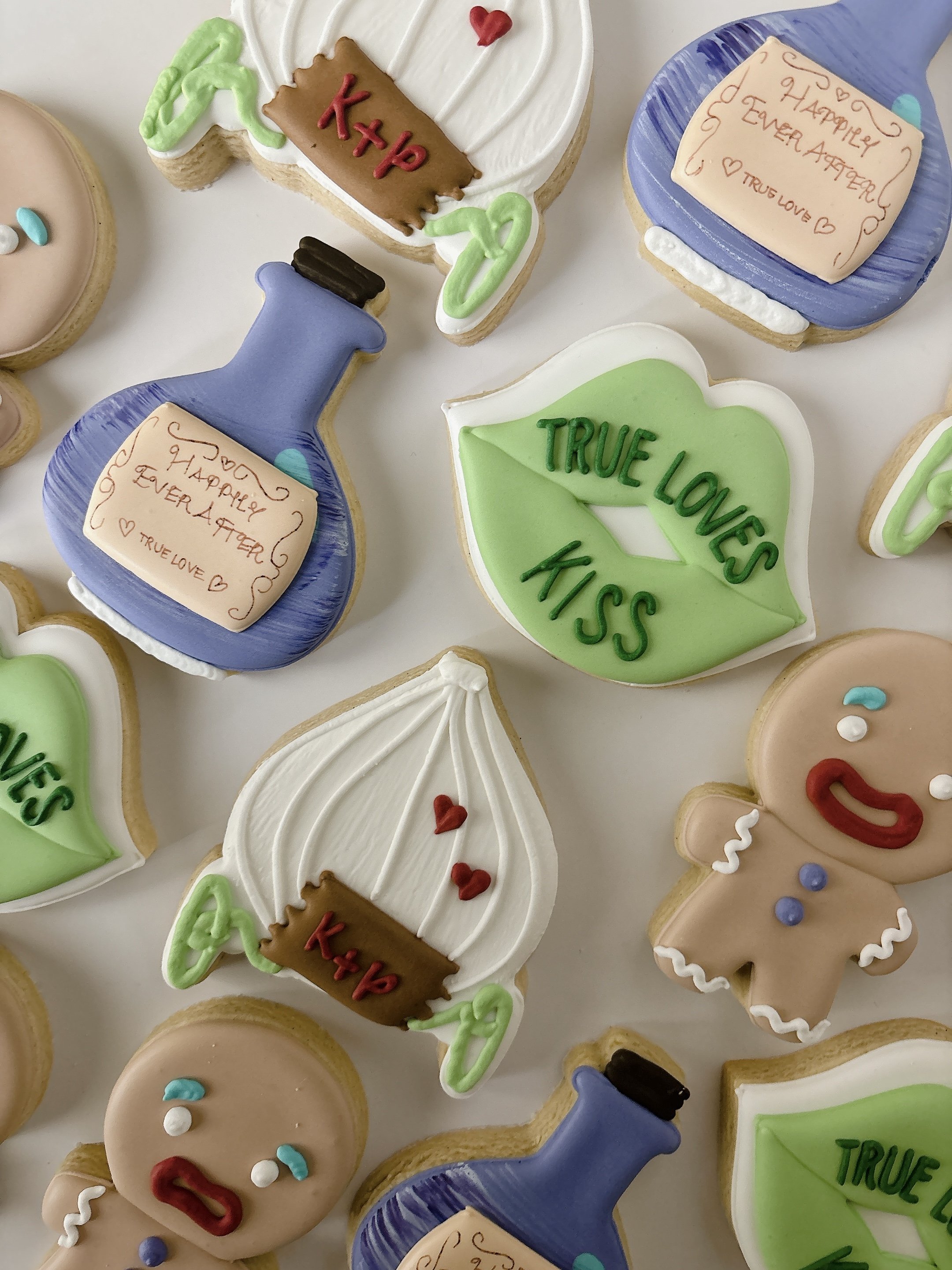 Assorted cookies decorated with colorful icing, including hearts, a knight helmet, and speech bubbles with messages like "True Love KISS," "Happy Ever After," and "K+P."