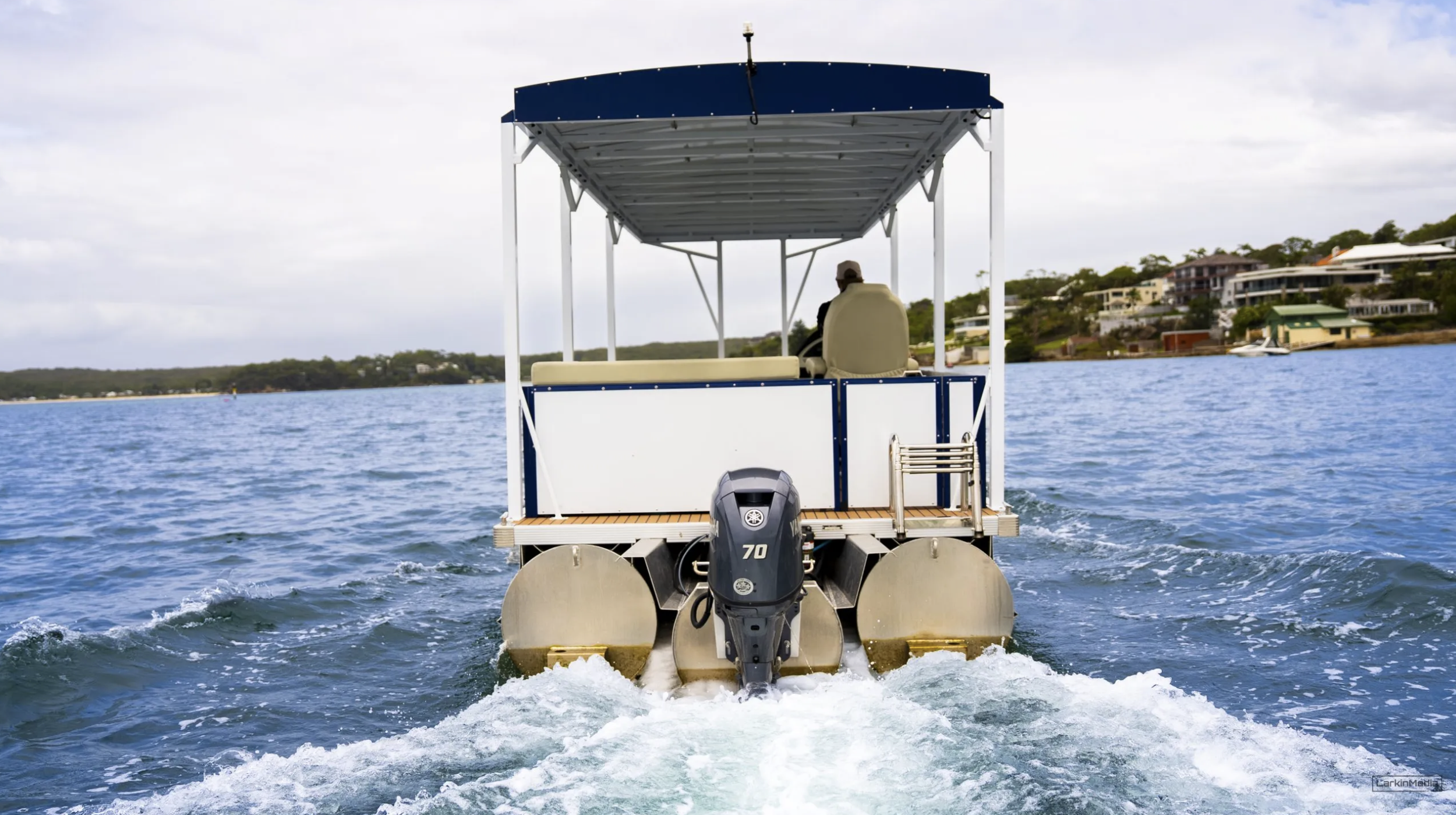 A small motorized boat on a body of water with houses and trees on the shoreline in the background.
