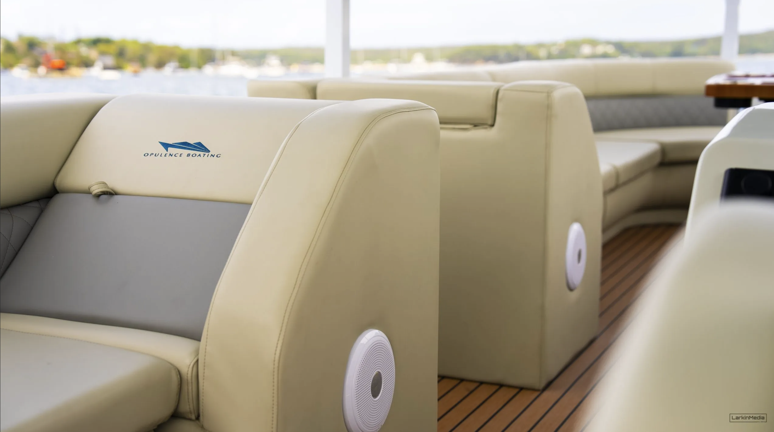 Interior of a boat with cream-colored seating, ocean view with boats and water in the background, and a logo that reads 'Opulence Boating' on one of the seats.