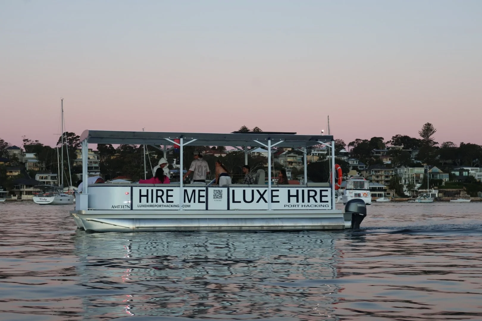Luxe Hire boat cruising Port Hacking at golden hour with guests aboard and the shoreline in the background.