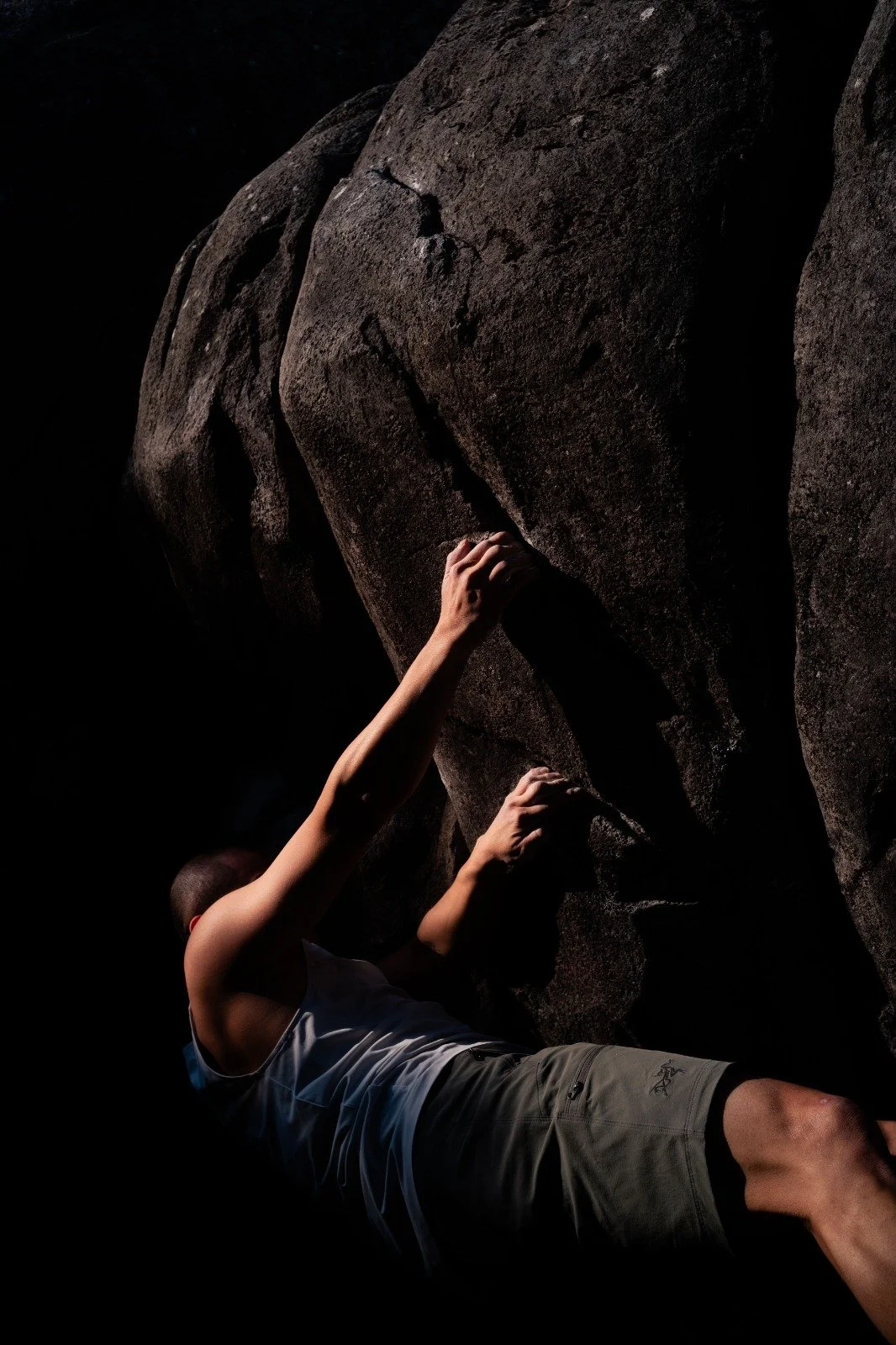 A person bouldering on a large rock formation in darkness.