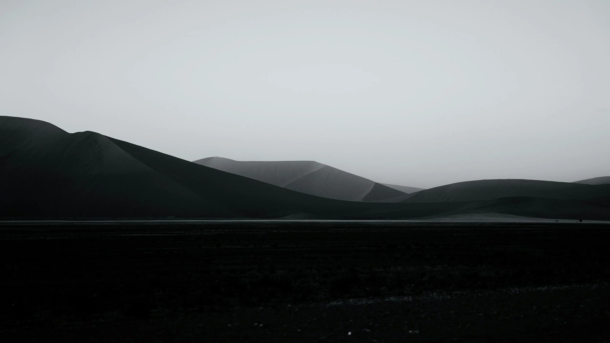 A landscape of rolling hills or mountains in grayscale with a cloudy, overcast sky.