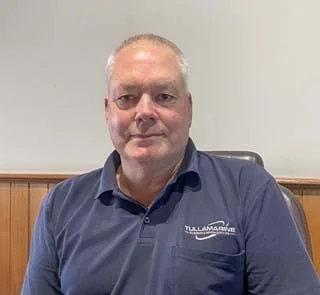 Older gentleman sitting at his desk wearing a company polo shirt