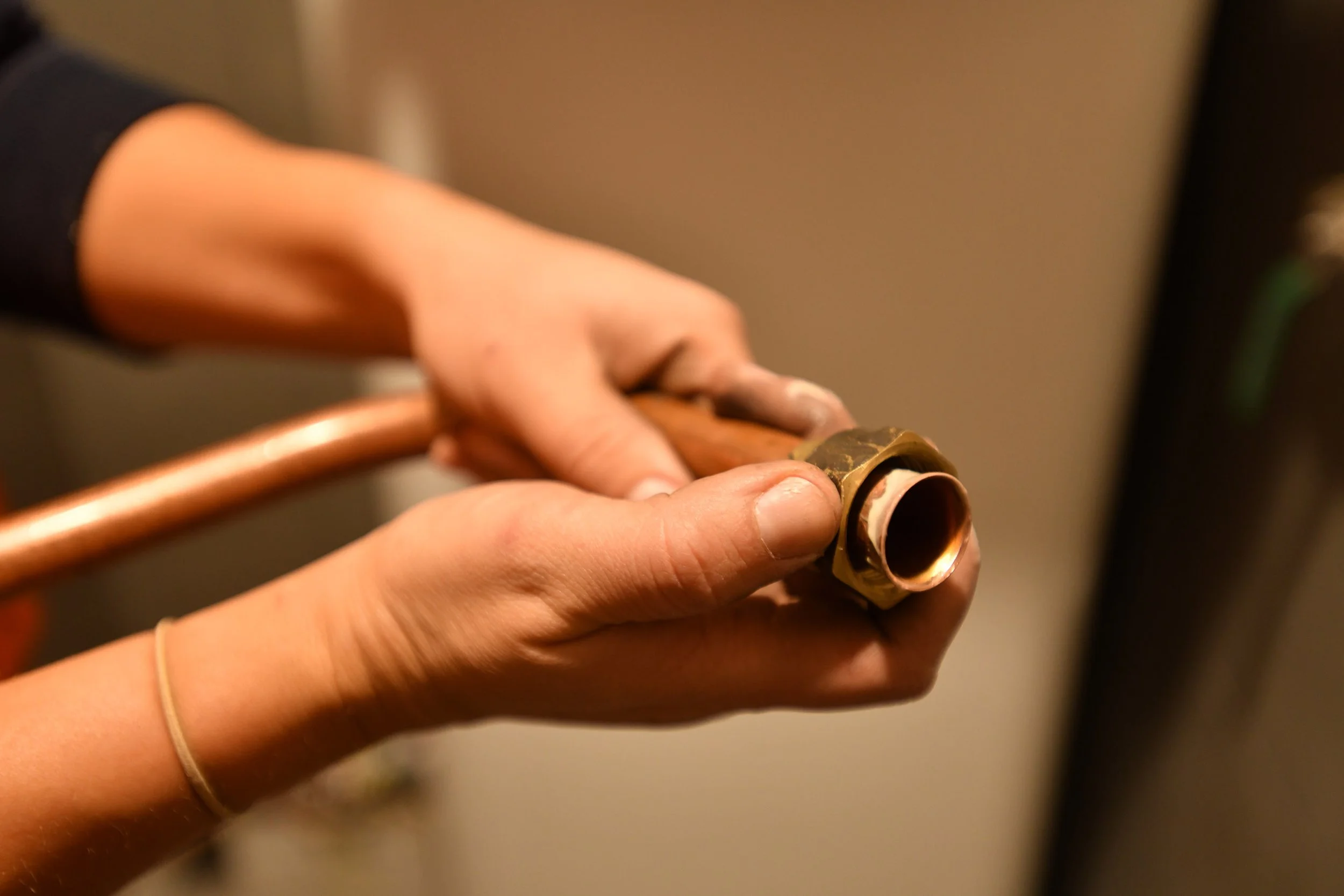 Close-up of a person's hand holding a copper pipe fitting.
