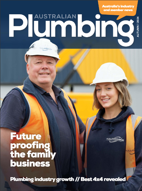 Two people wearing hard hats and safety vests smiling outdoors, with construction equipment in the background, on the cover of Australian Plumbing magazine.