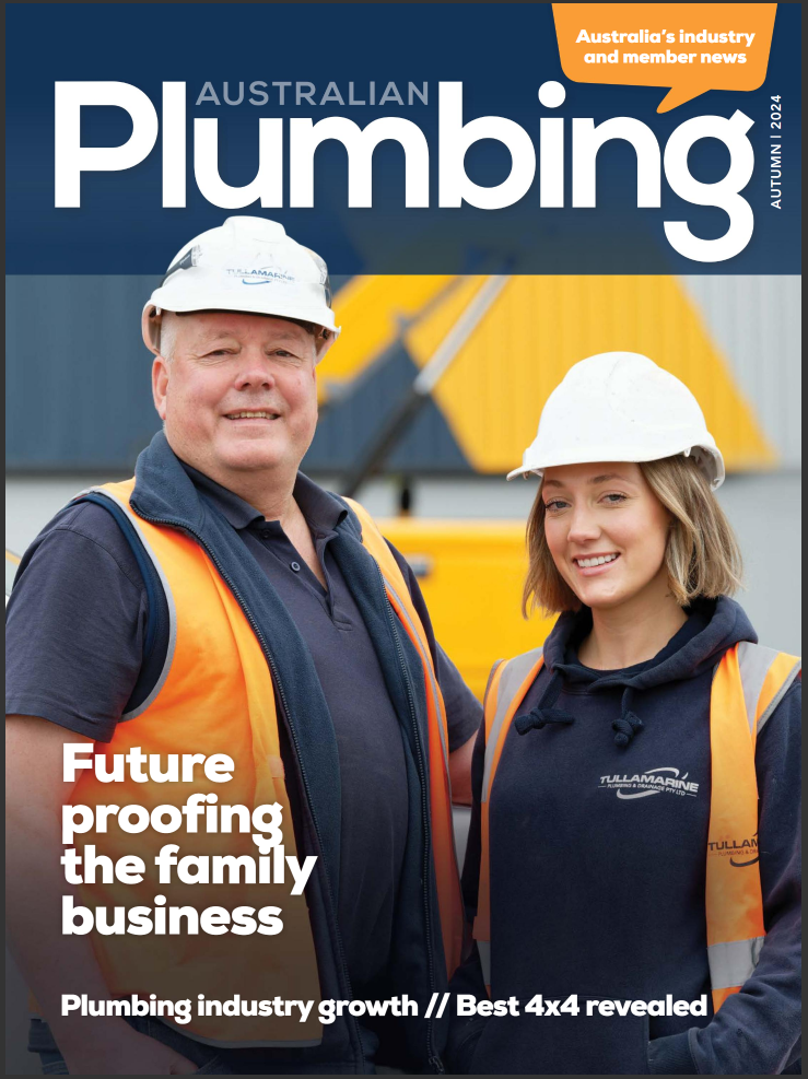 Cover of Australian Plumbing magazine featuring a man and woman wearing safety helmets and reflective vests, smiling, with plumbing equipment in the background.