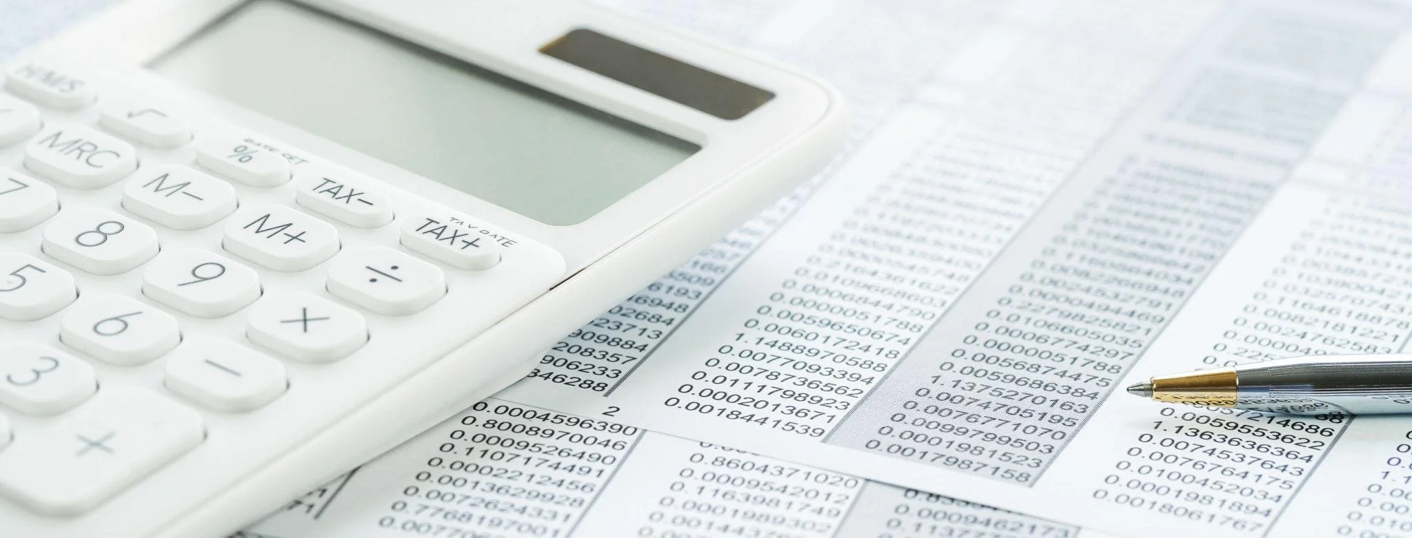A white calculator and a pen on printed financial data and numbers.