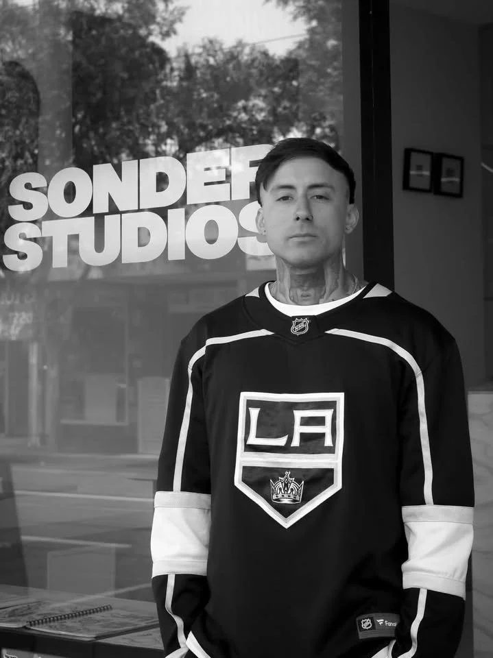 A young man with tattoos wearing a Los Angeles Kings hockey jersey, standing outside SONDER STUDIOS.