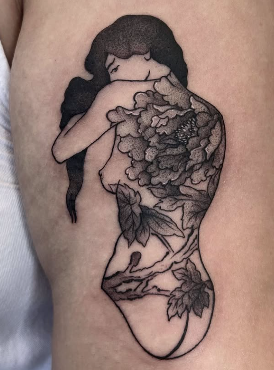 Tattoo of a woman hugging herself with floral and landscape designs integrated into her body, including leaves, branches, and clouds.