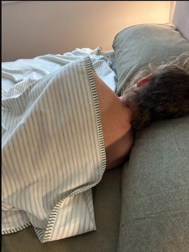 Person sleeping on a bed, covered with a striped blanket, with their head resting on a pillow.