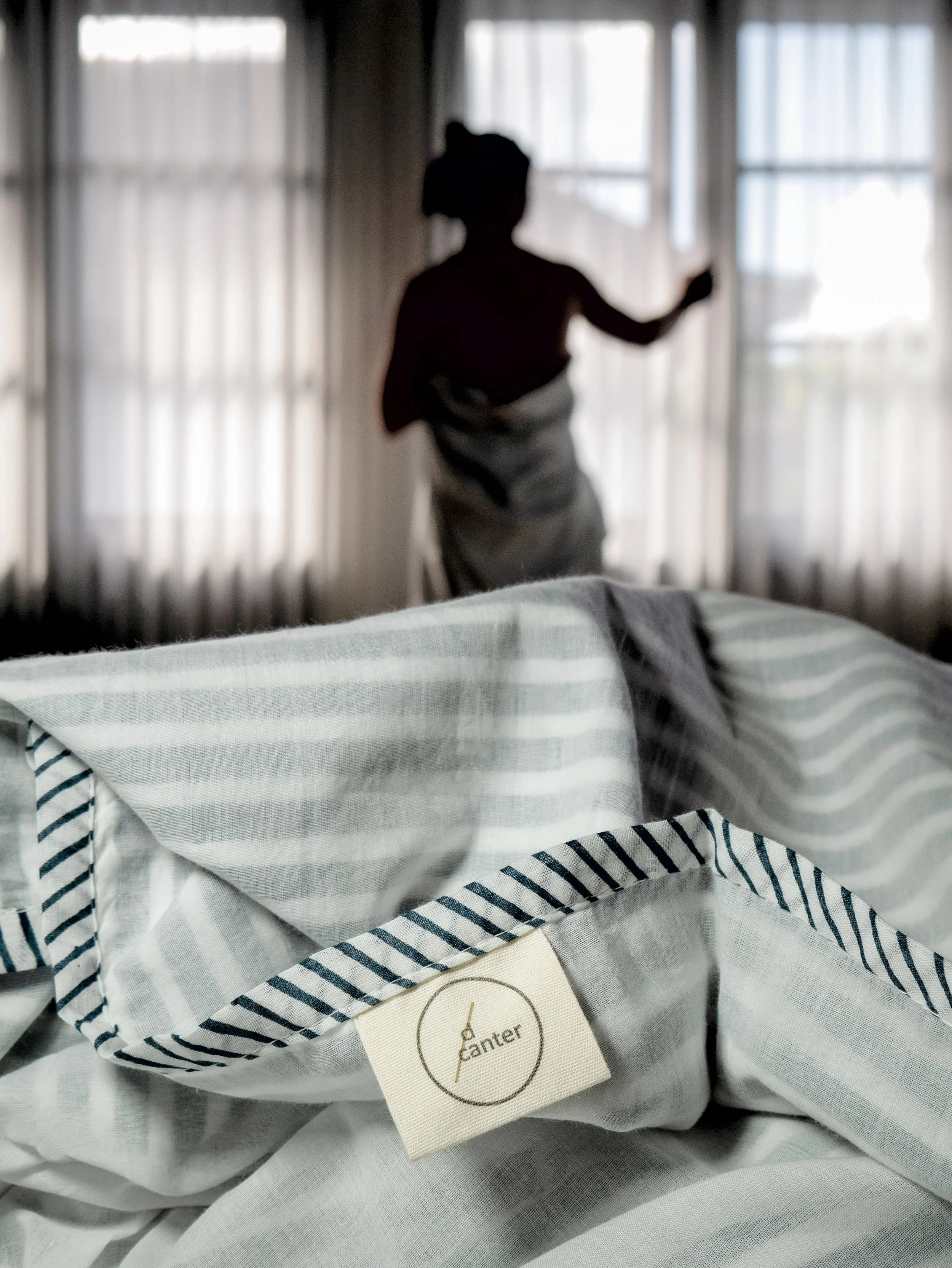 Person arranging a d/canter cotton muslin blanket in a softly lit bedroom