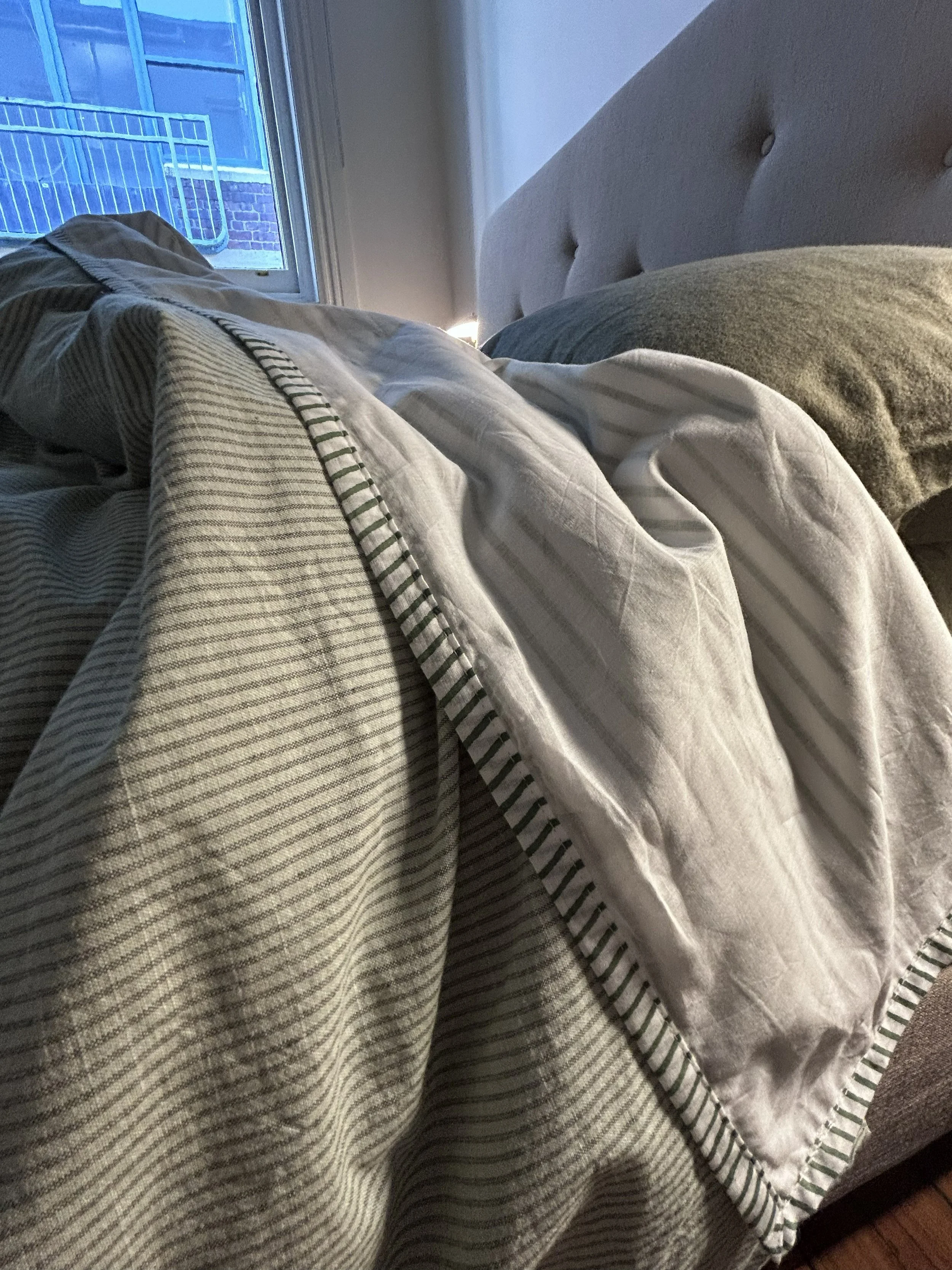 Close-up of a bed with striped sheets and a pillow near a window with a balcony outside.