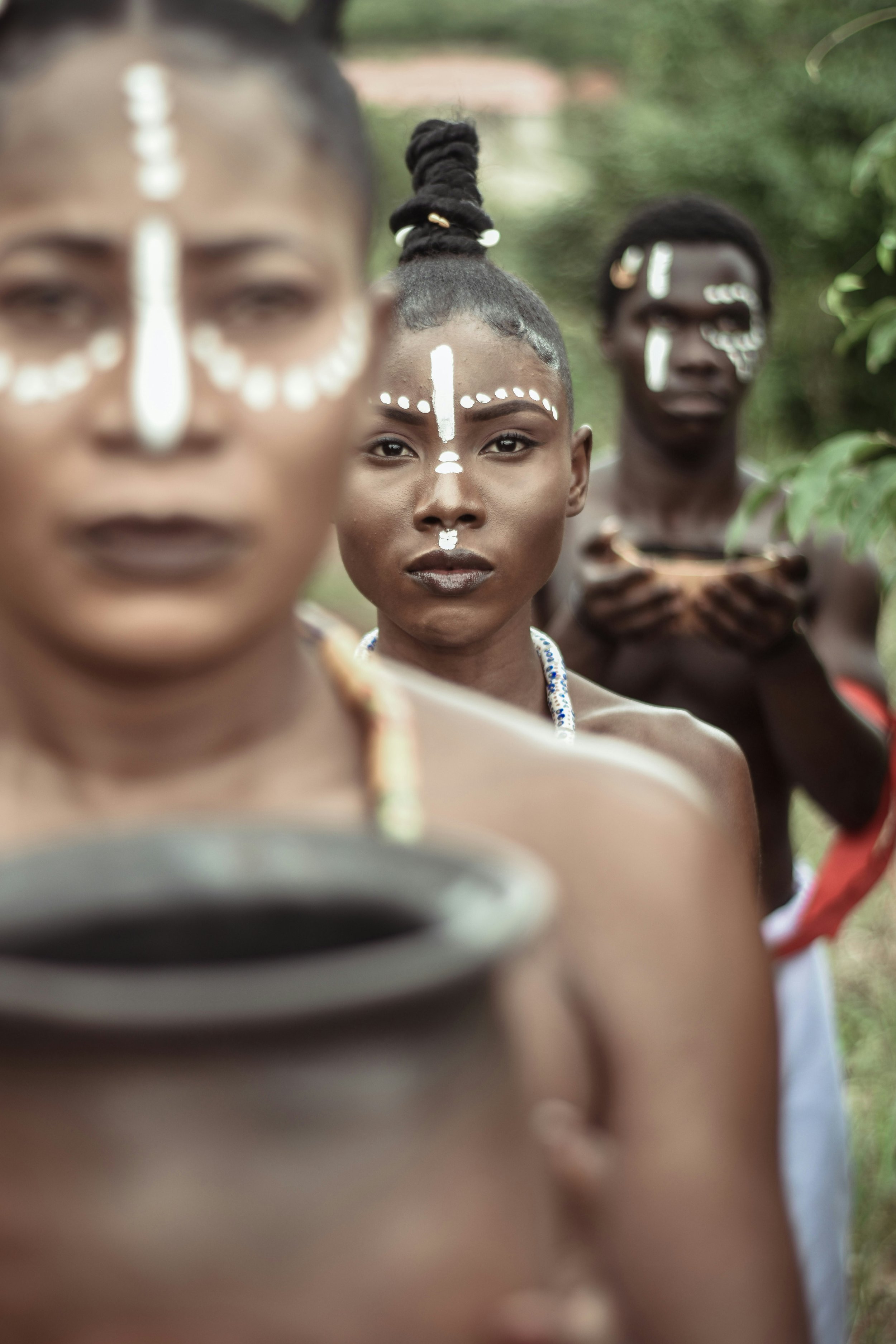 Three Indigenous women with face paint. The woman in the center is looking directly at the camera, while the women on the sides are blurred.