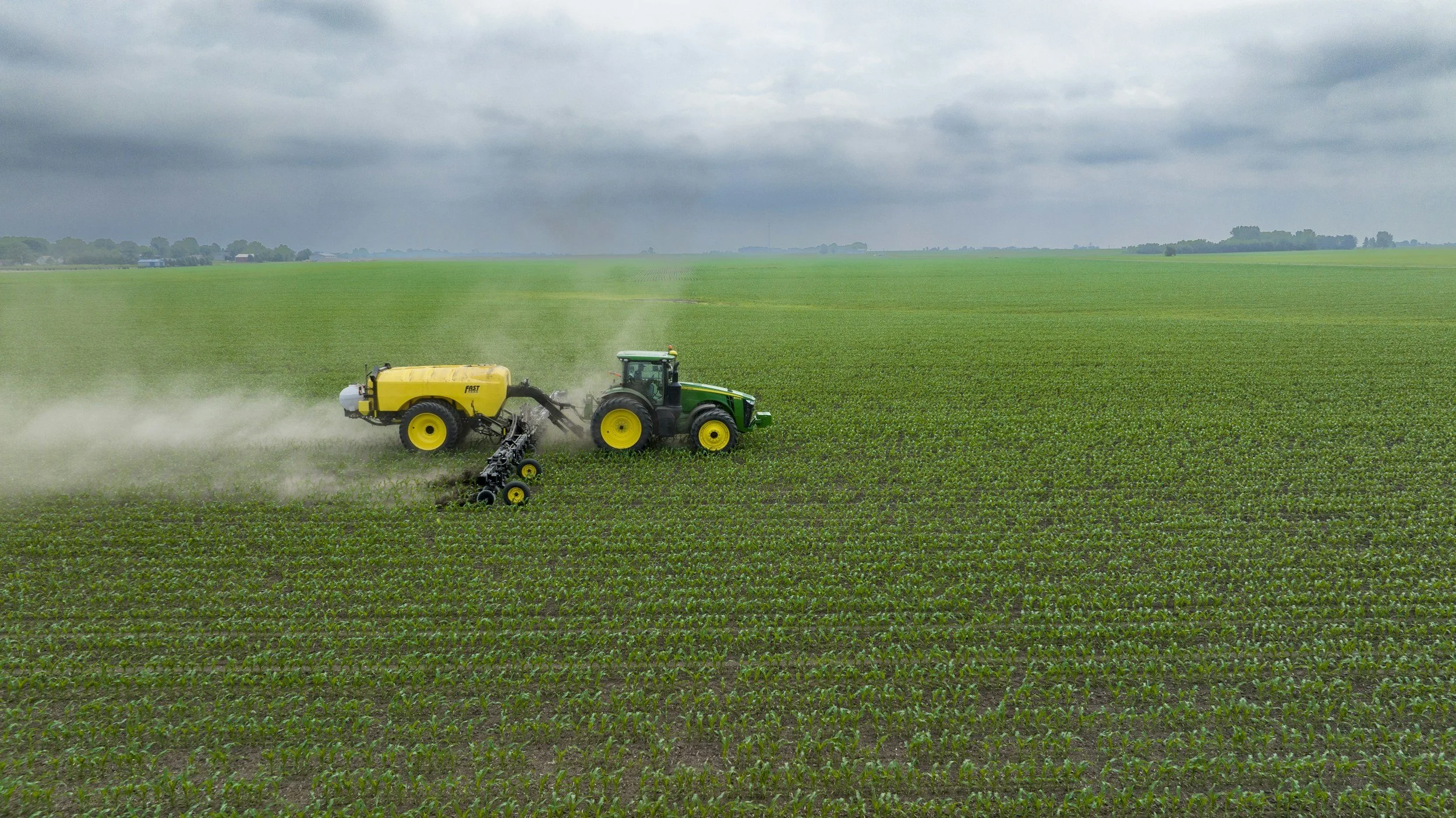 A tractor spraying crop fields on a cloudy day.