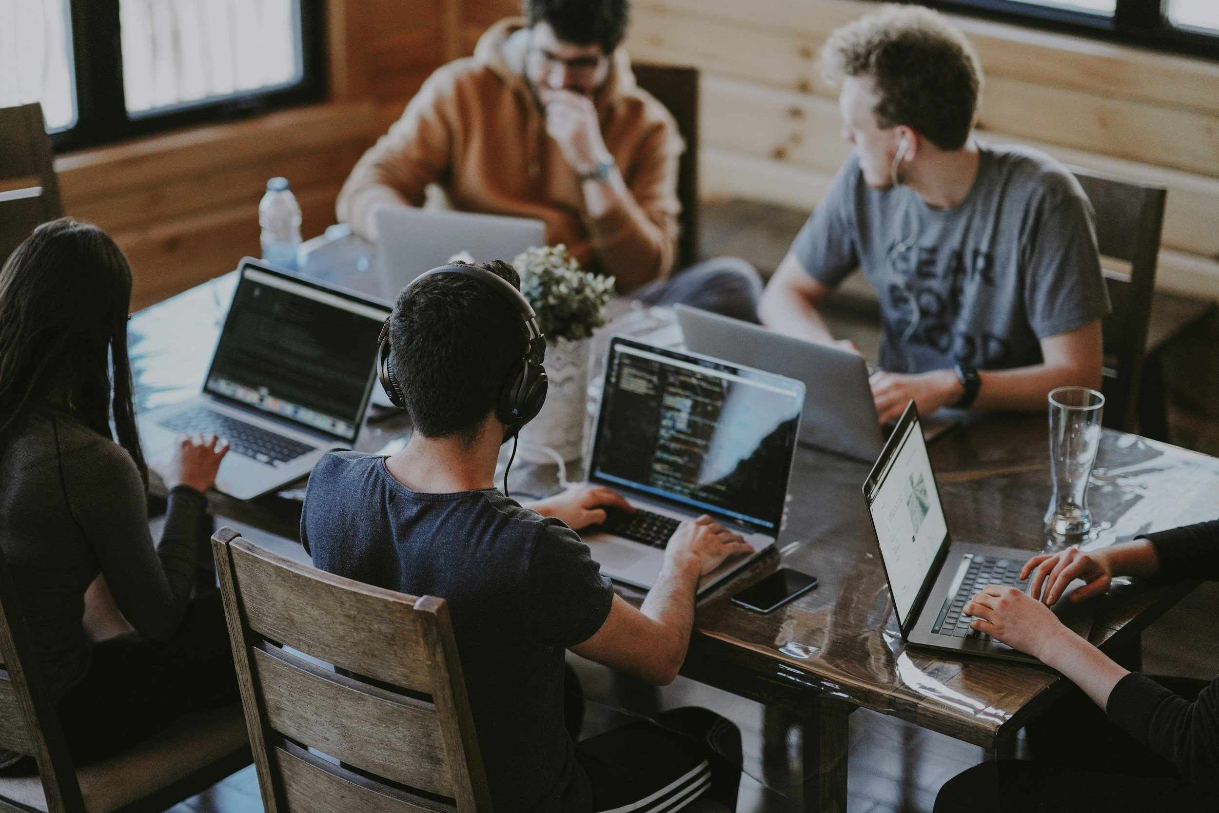 A group of people working on laptops around a wooden table in a cozy, wood-paneled room.