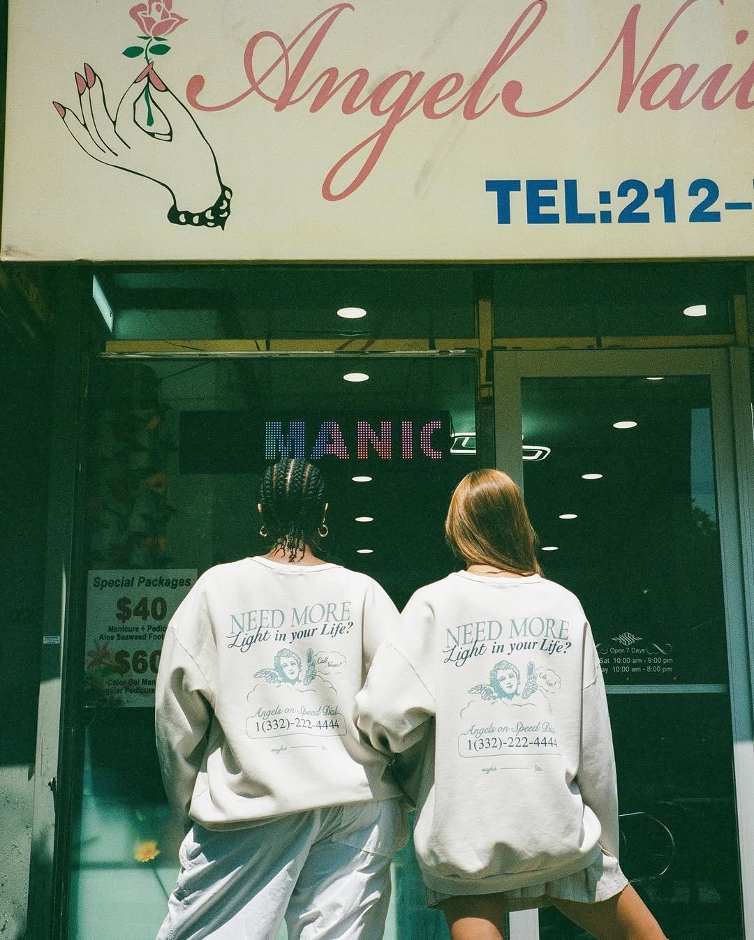 Two women wearing sweatshirts with a logo and text standing in front of a nail salon entrance.