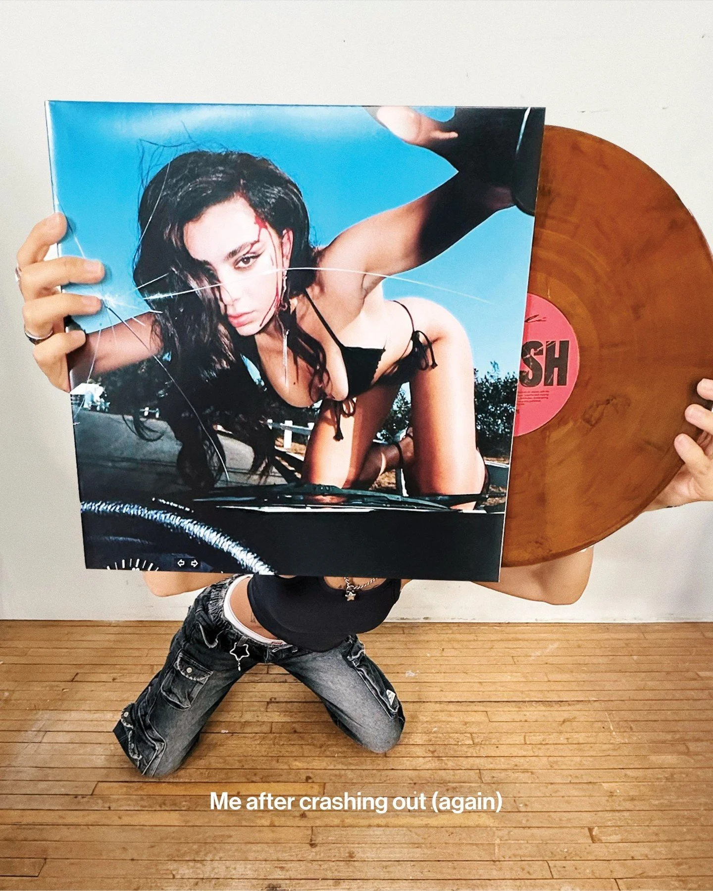 A person holding a vinyl record and a album cover, which features a woman with dark hair and makeup, in a crouched position. The caption says, "Me after crashing out (again)."