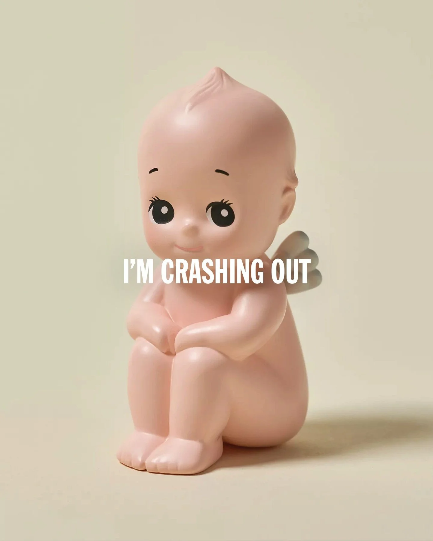 A small, nude figurine with cartoon-like facial features, holding a tiny object, with the text "I'M CRASHING OUT" overlaid.