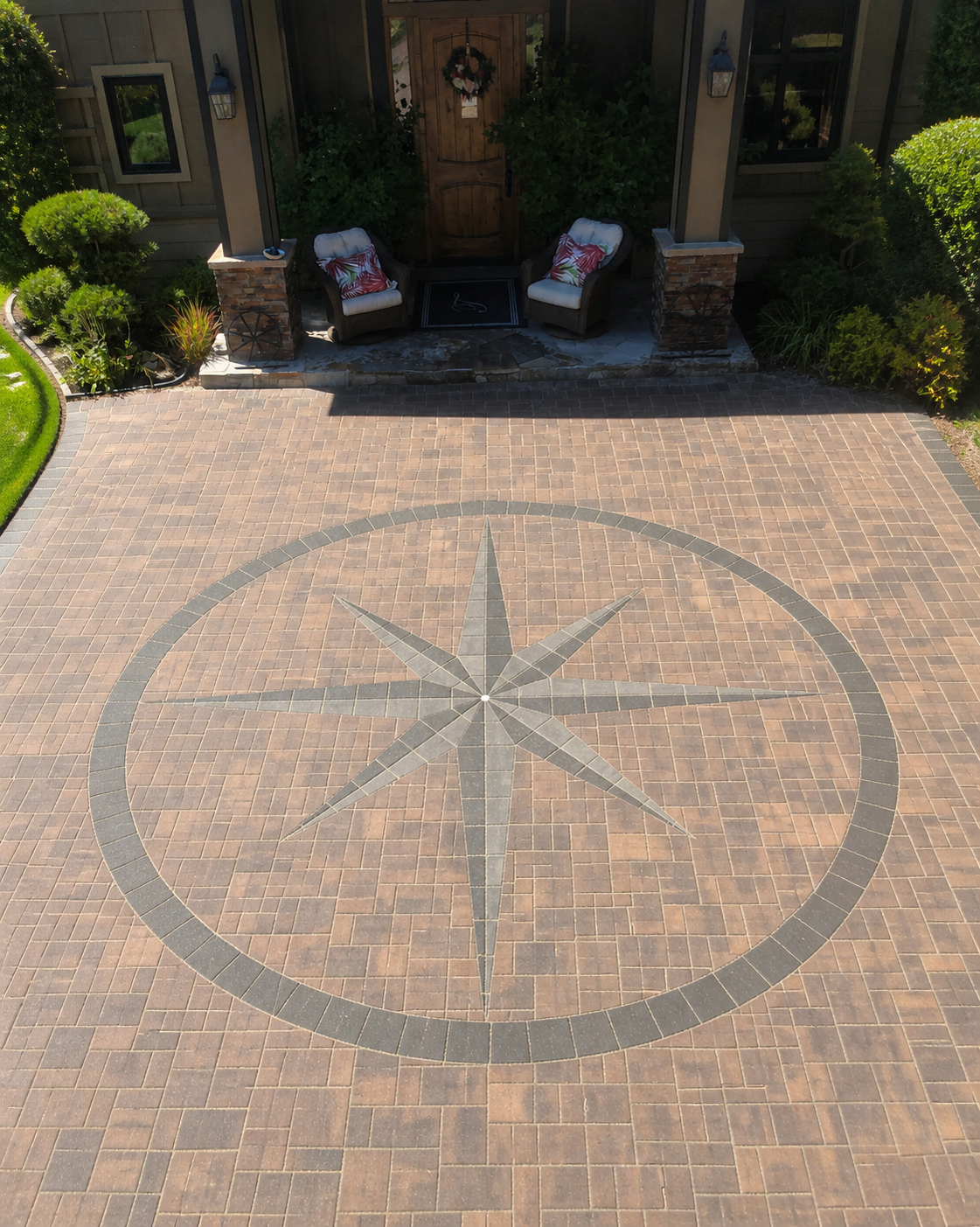 A decorative paved courtyard with a large compass rose pattern in the center, in front of a house entrance with two chairs, pillows, and a door decorated with a wreath.