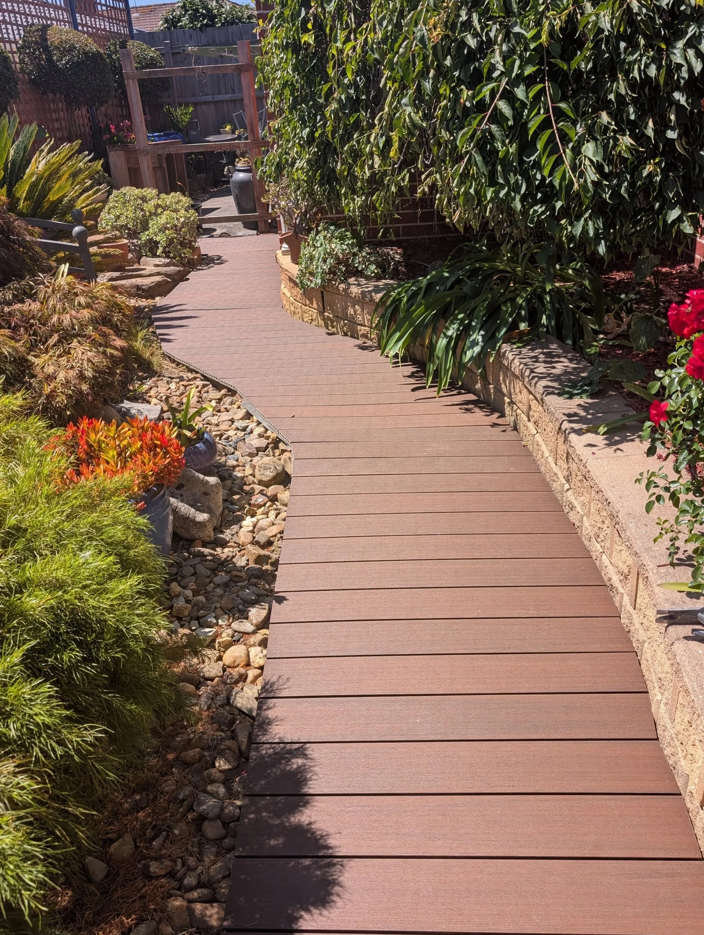 A backyard with a wooden pathway, plants, and shrubs, enclosed by a fence and trellis. elevate property maintenance and repairs home care landscaping melbourne outer east and yarra valley deck build and repair pergola install garden care