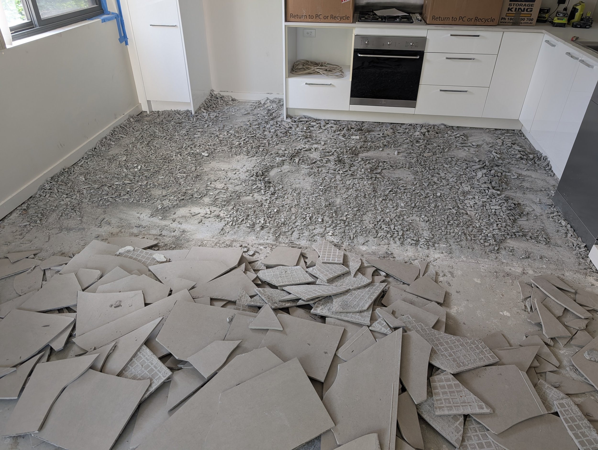Kitchen renovation site with broken tiles and debris on the floor, appliances and cardboard boxes on countertops. elevate property maintenance and repairs home care landscaping melbourne outer east and yarra valley tile removal