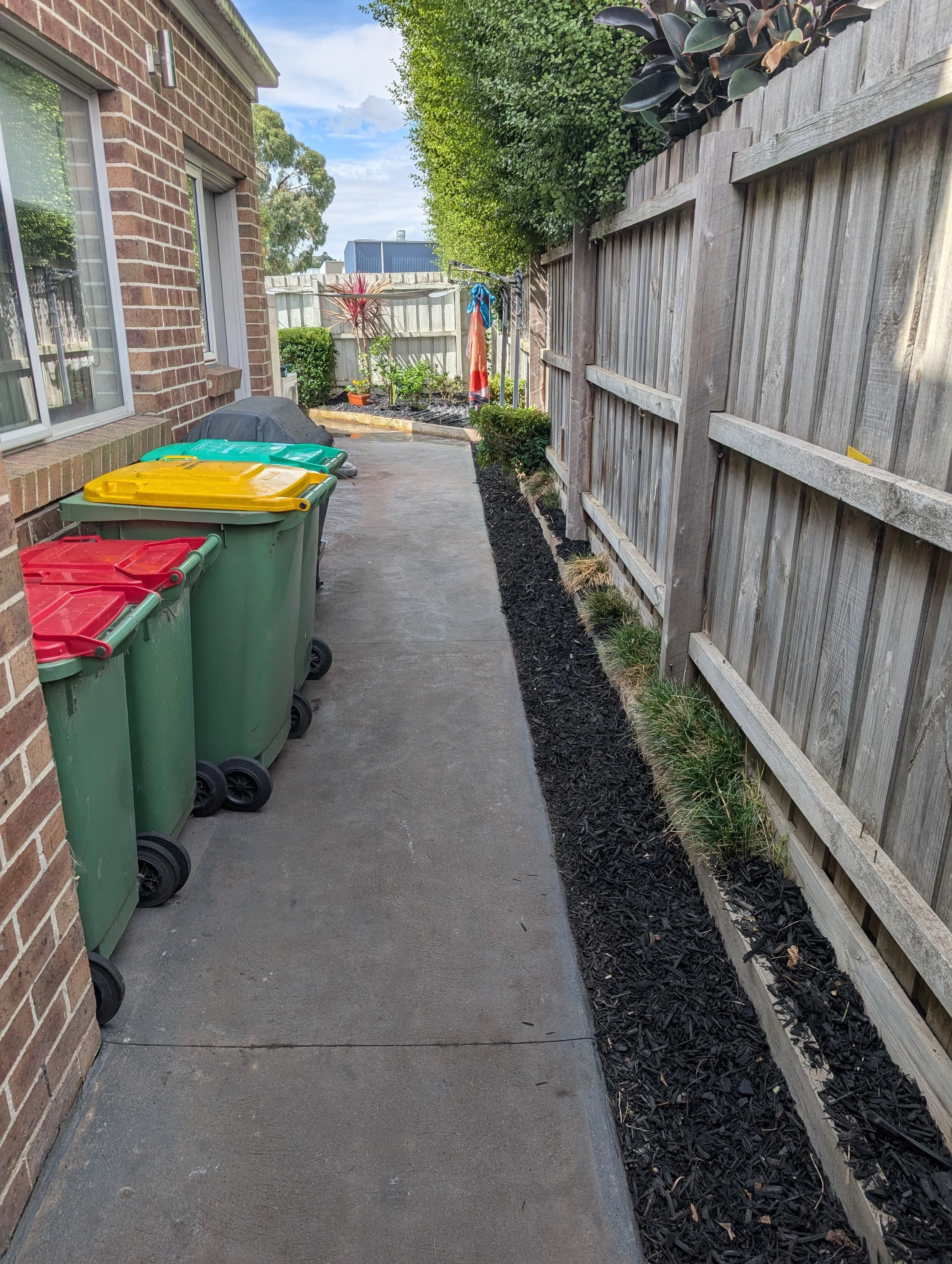Backyard pathway with trash bins, a fence, some plants, and trees. elevate property maintenance and repairs home care landscaping melbourne outer east and yarra valley weeding mulching pre-sale care